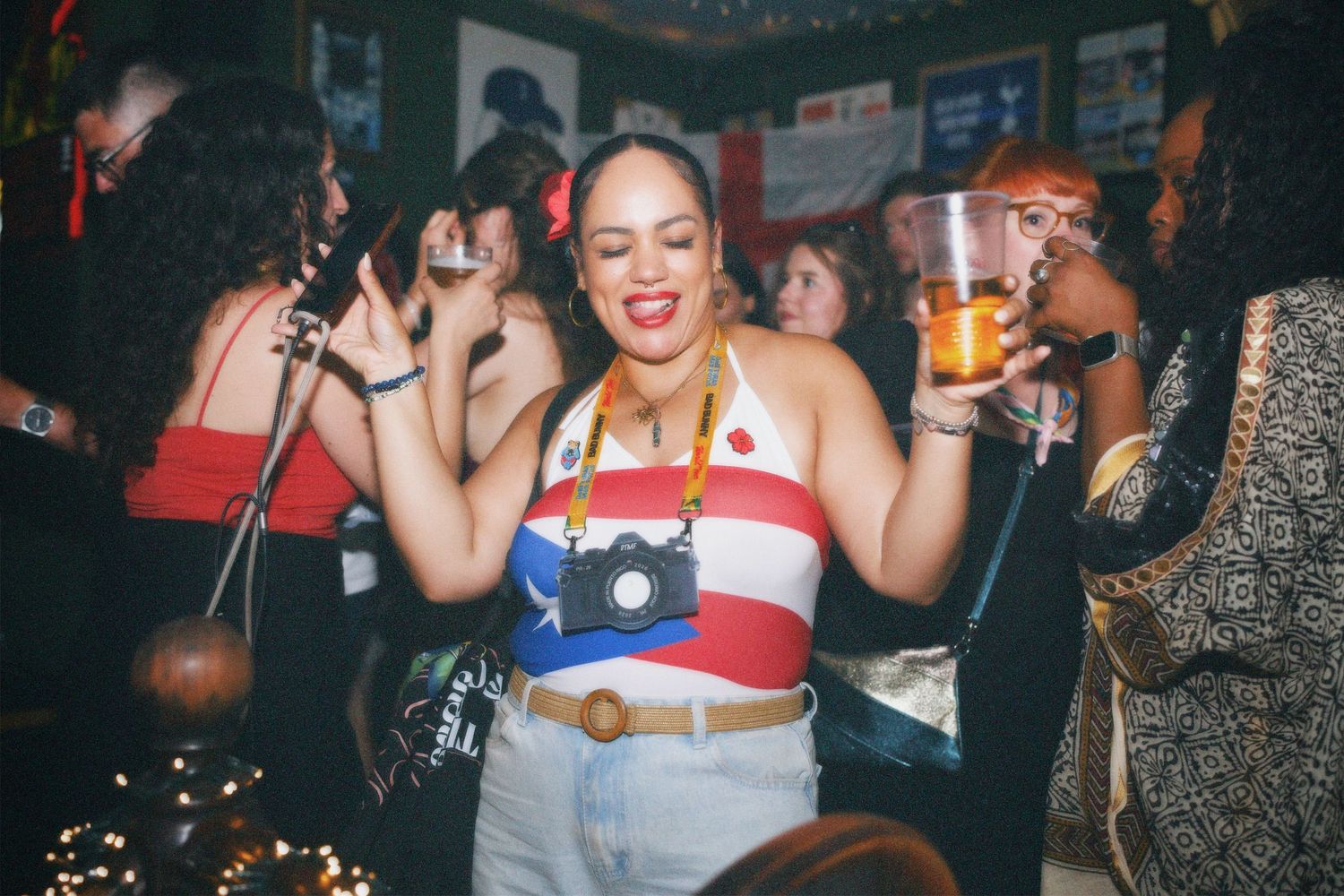 Woman in Puerto Rico flag top holding drink at lively London bar by ARIETA Studios.