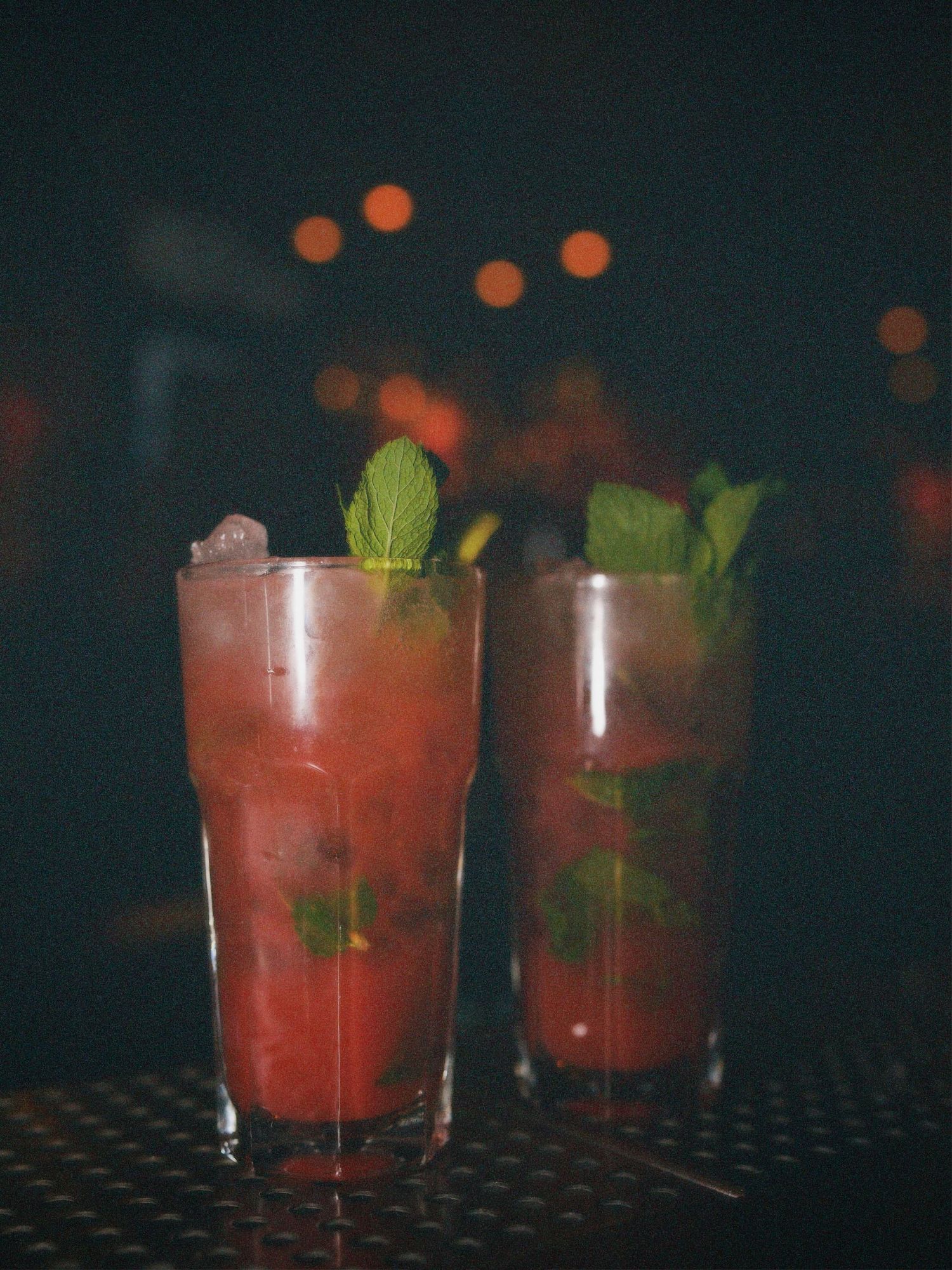 Macro shot of two red cocktails garnished with fresh mint on a dark bar surface. Nightlife branding photography by ARIETA Studios.