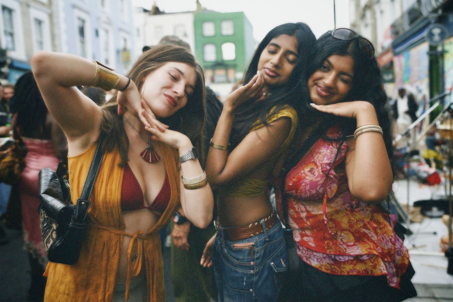 Candid street portrait of three women in festival crop tops smiling and posing together.