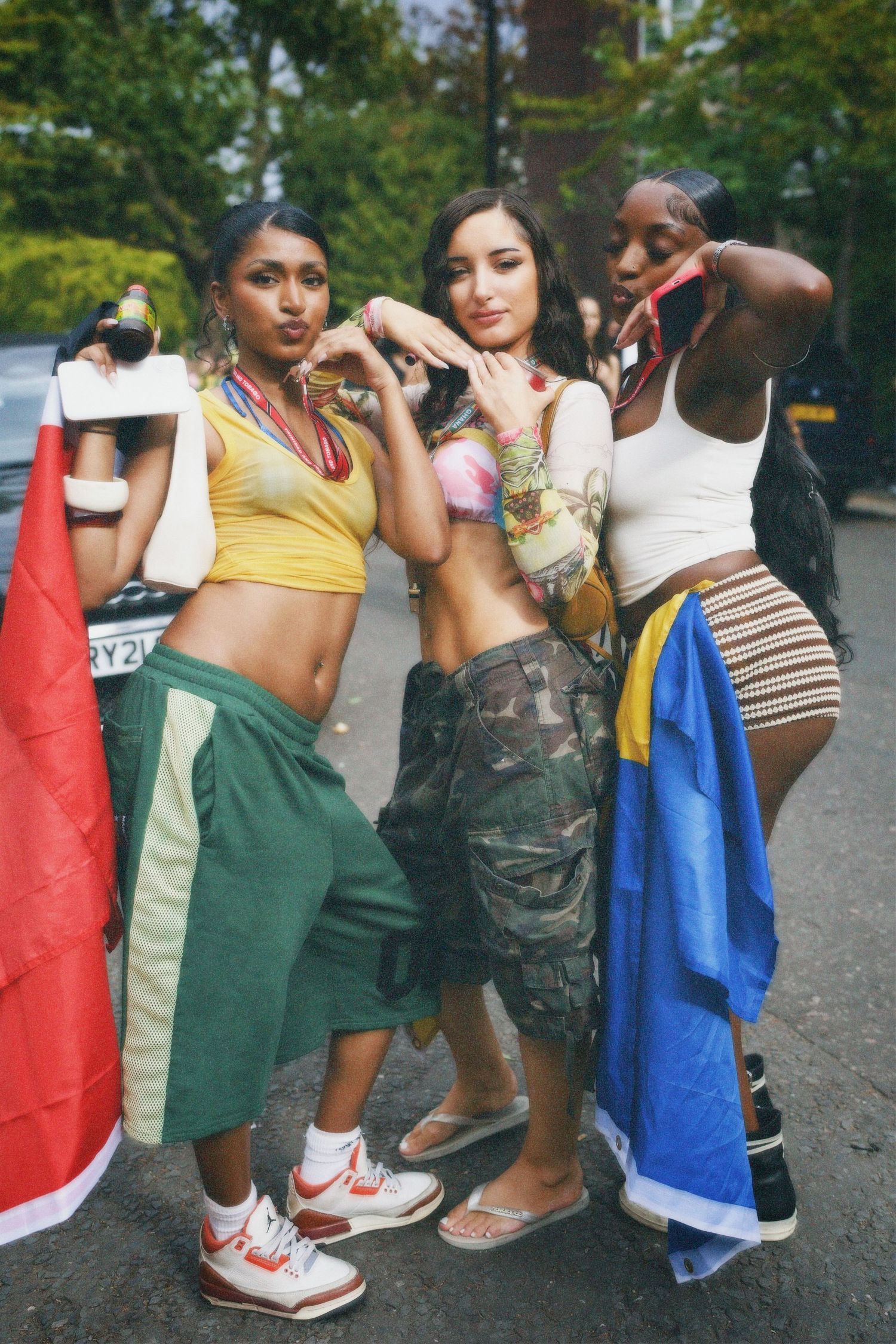 Three young women posing in summer festival fits on the road at Notting Hill Carnival.