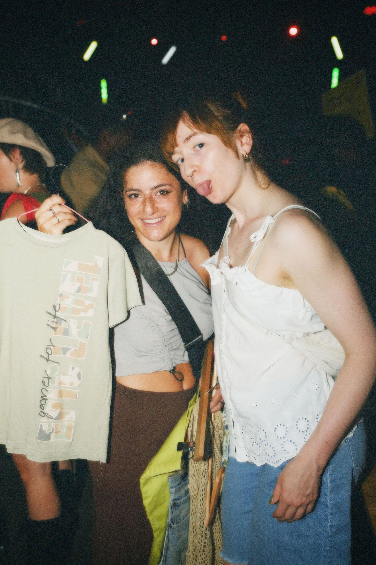 Two friends holding up a thrifted graphic tee and smiling inside the Fashion For Future swap event venue