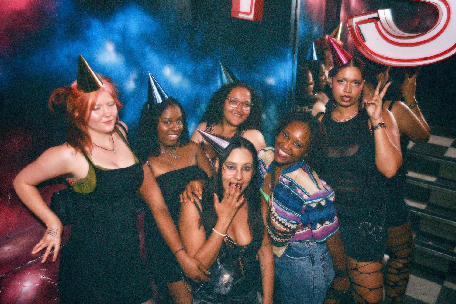 Group of friends wearing party hats posing at a London nightlife event for Neon Nostalgia by ARIETA Studios.