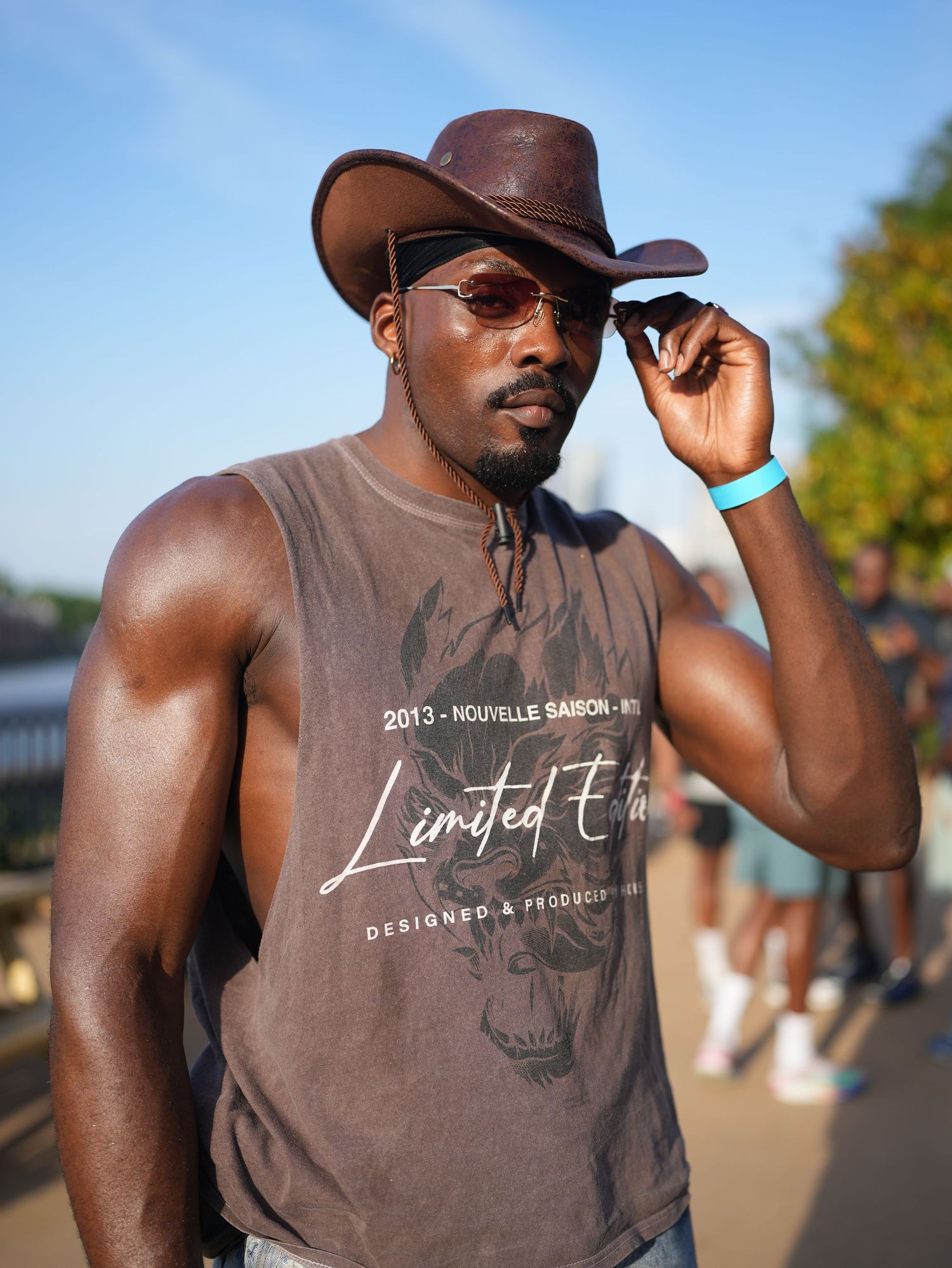 Outdoor portrait of a stylish man wearing a brown leather cowboy hat and sunglasses during golden hour.