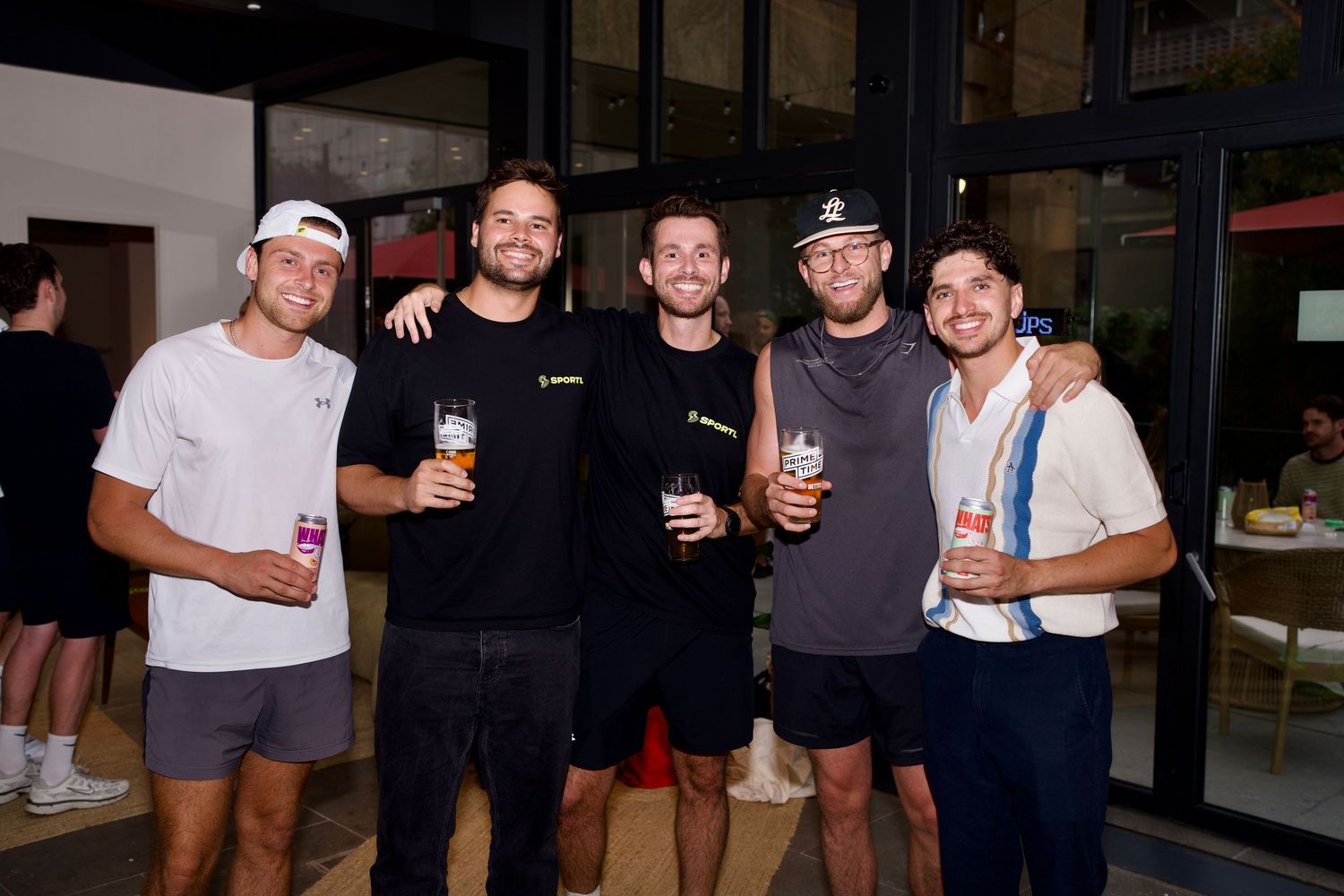 Five men smiling together while holding beers and WhatsUp Vodka Iced Tea cans at a London event. Photo by ARIETA Studios.