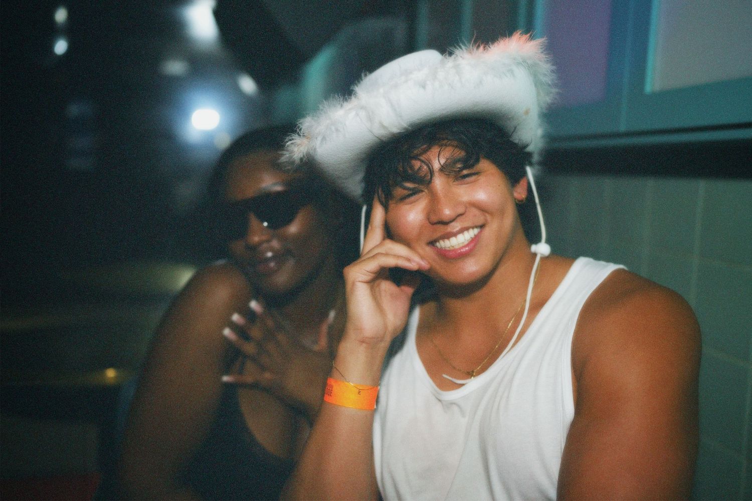 Woman wearing a white cowboy hat smiling directly at the camera at a party.
