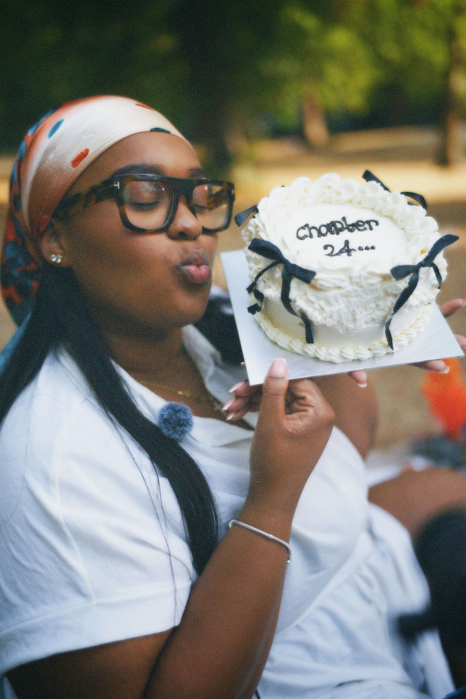 Chantelle wearing a headscarf and glasses outdoors, smiling proudly while holding up her decorated 24th birthday cake.