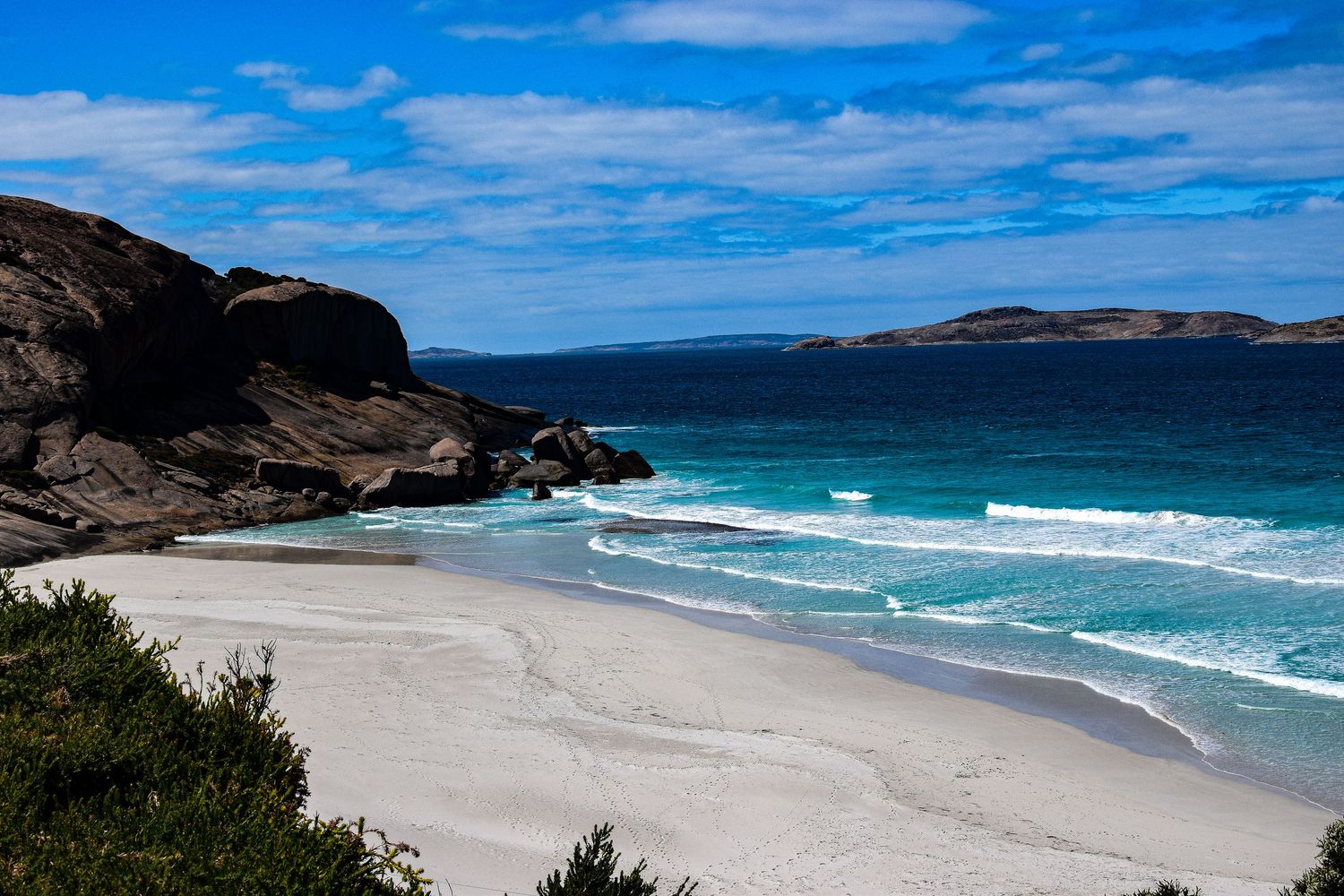 Pristine white sand beach with turquoise water and rocky coastline under blue sky.