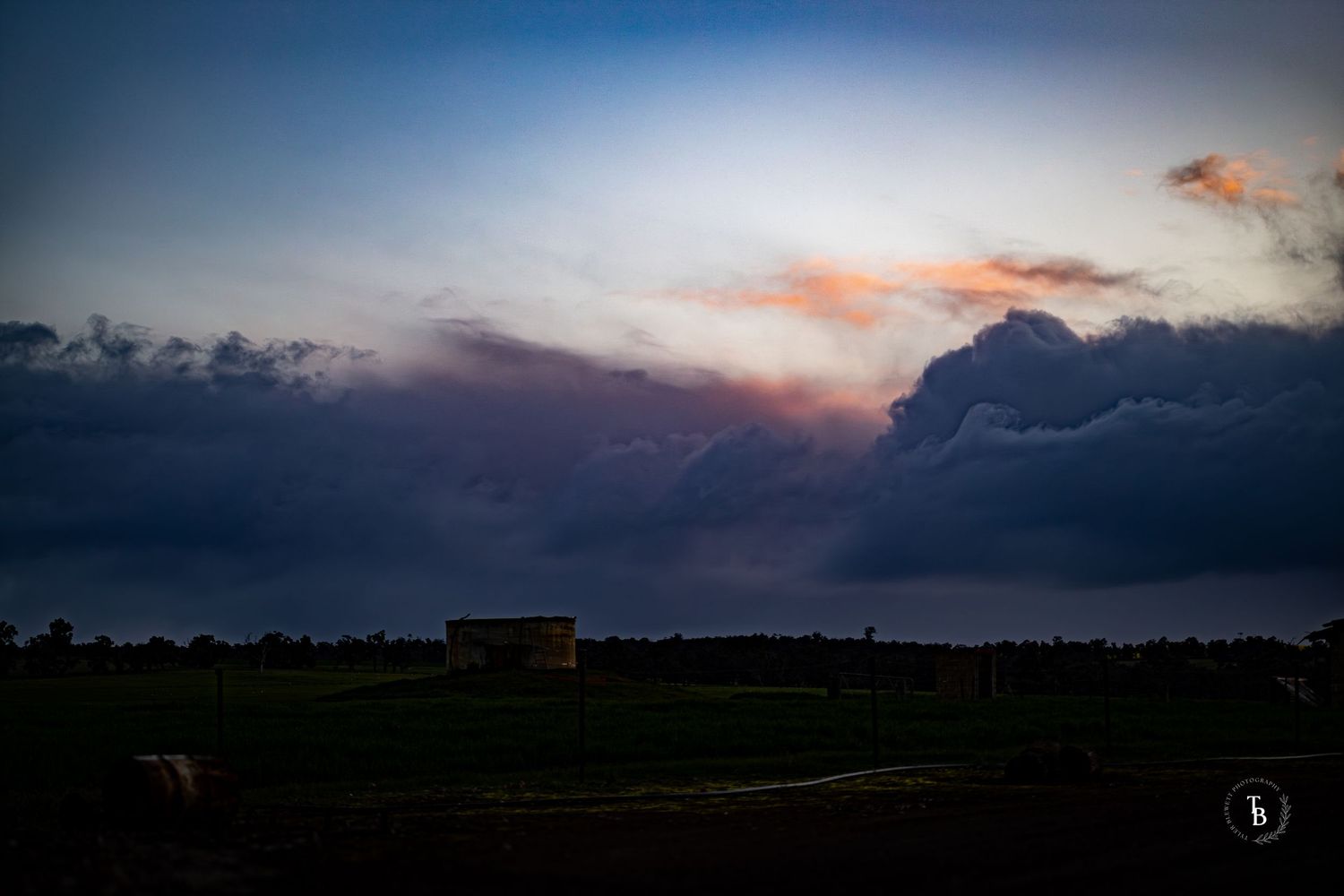 Dramatic sunset over flat farmland with dark storm clouds.