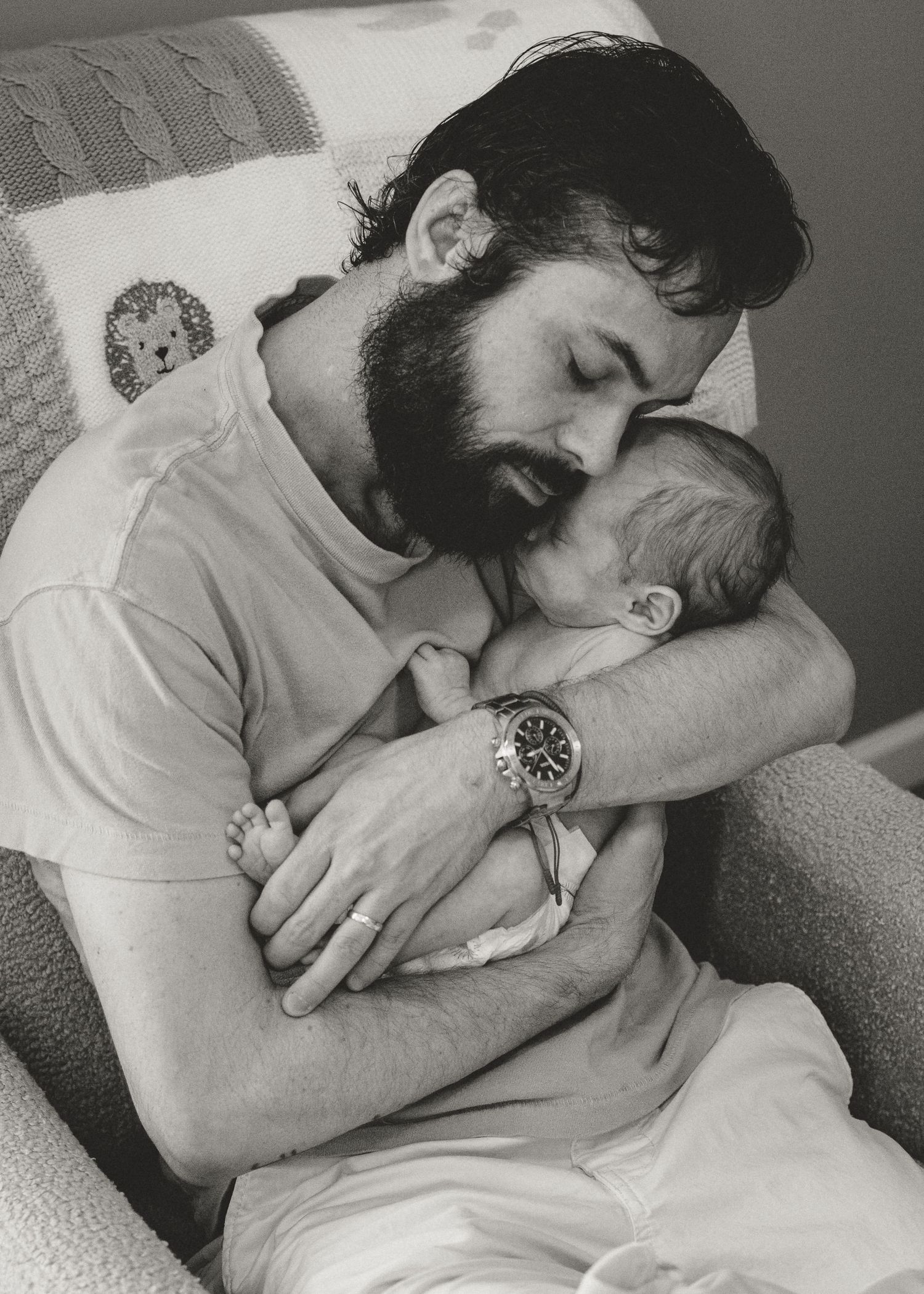 Bearded father tenderly kissing his sleeping newborn baby in black and white photo.