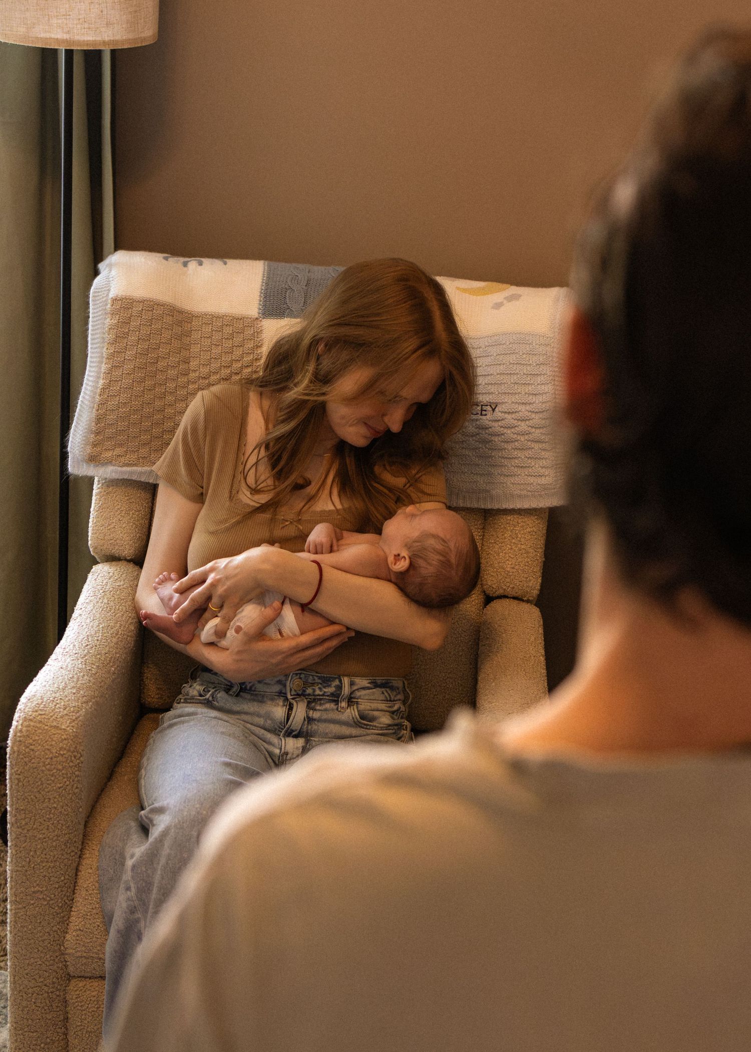 New mother sitting in recliner chair tenderly holding and bonding with her newborn baby.
