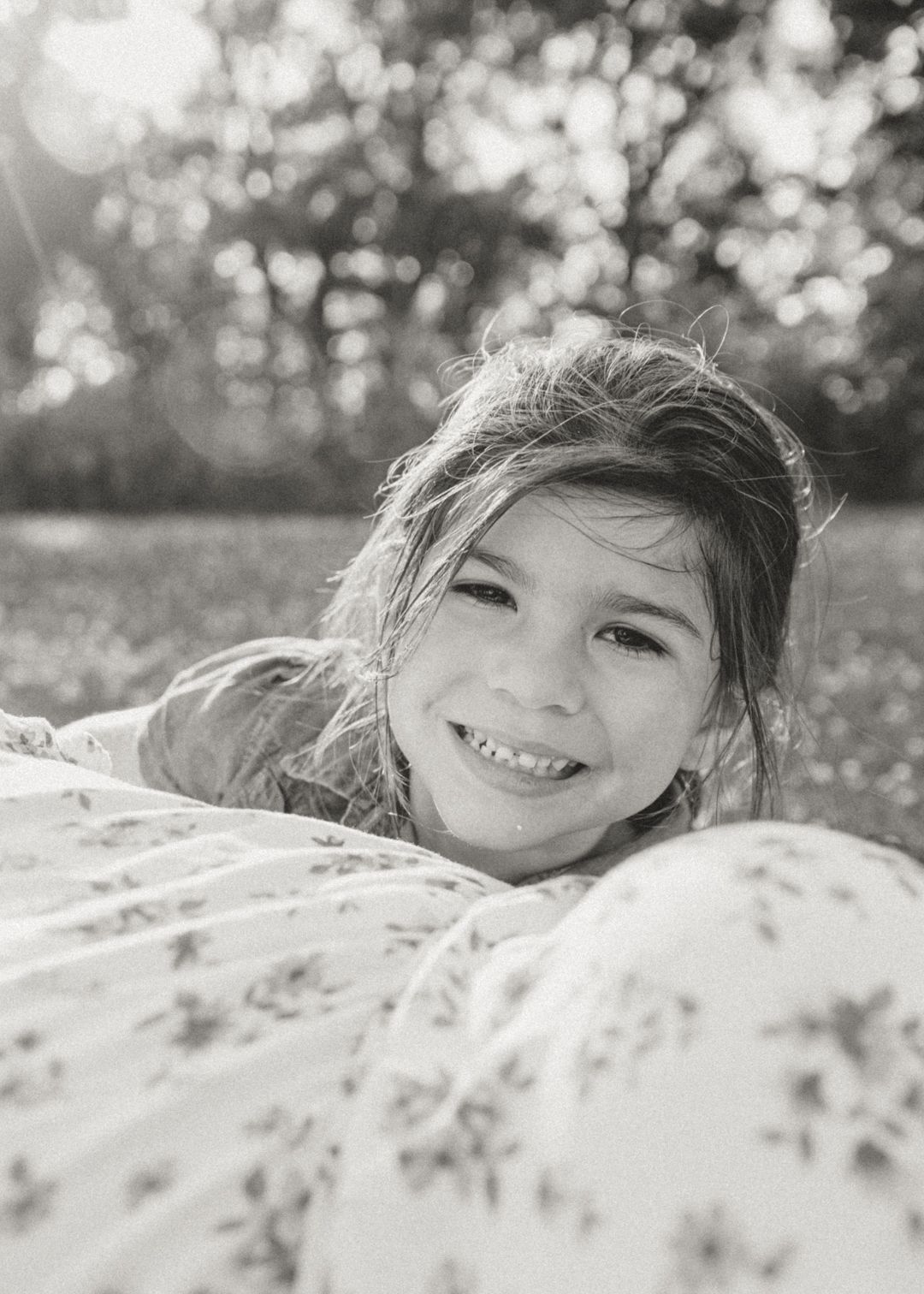 Smiling young girl lying on mom outdoors in black and white portrait photo.
