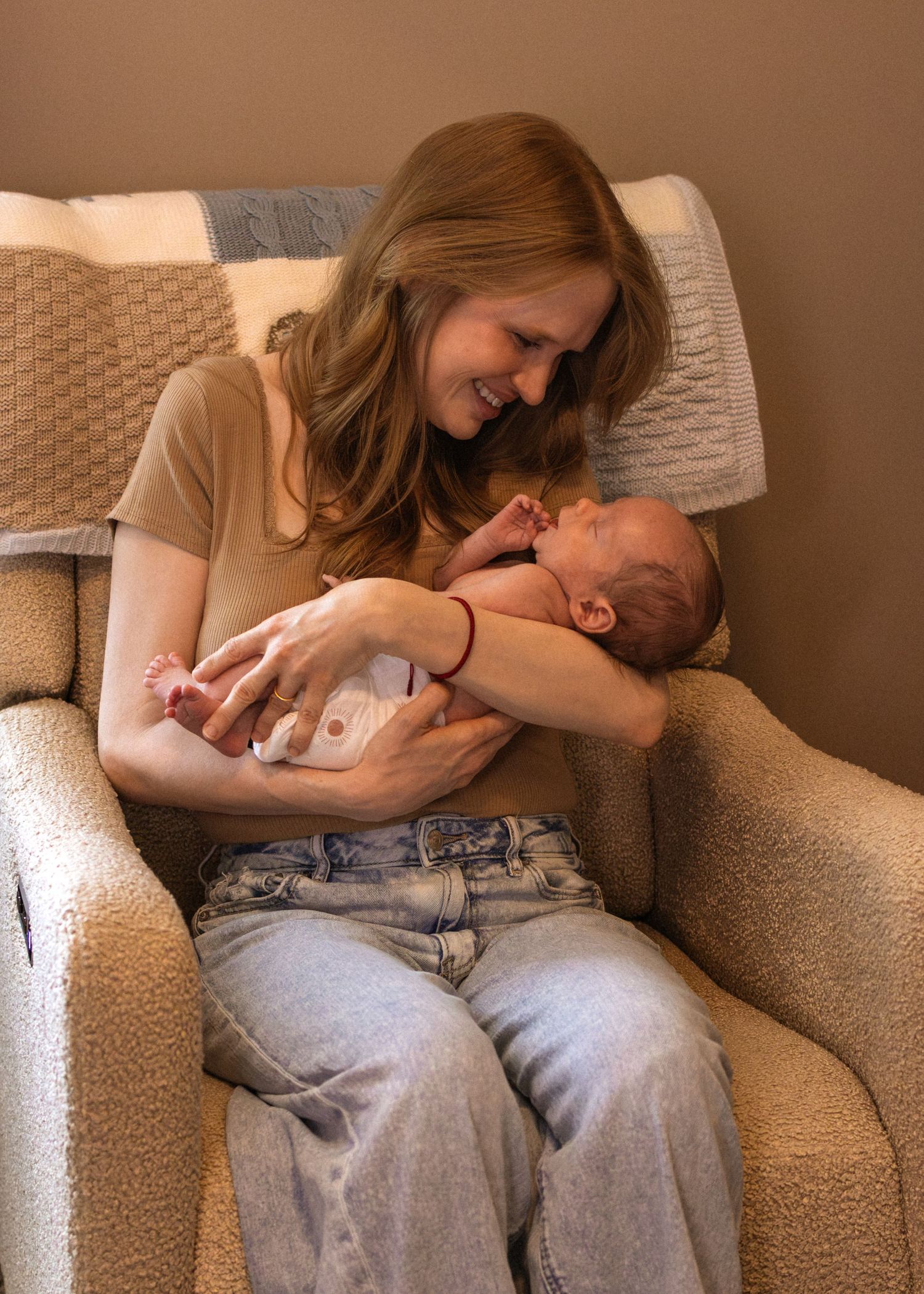 Smiling mother with red hair holds her newborn baby while sitting in a cozy armchair.
