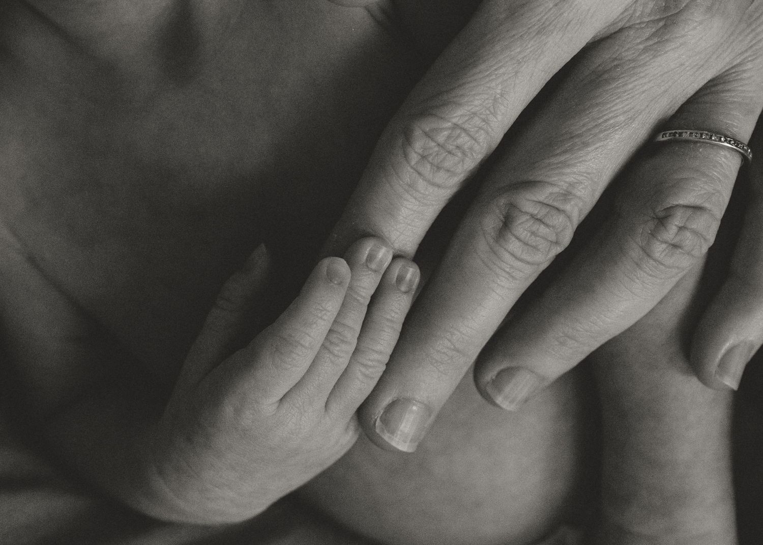 Black and white close-up of newborn baby hand resting on mothers hand with ring.