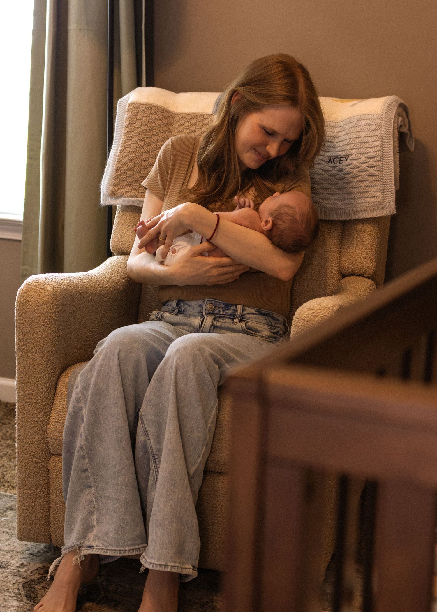 New mother sitting in nursery glider chair lovingly cradling her newborn baby.