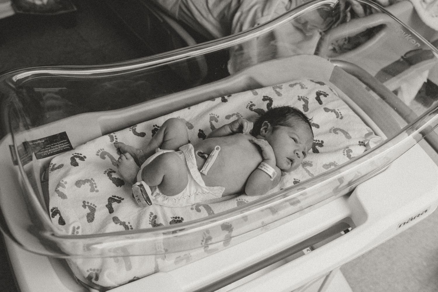 Black and white photo of a newborn baby resting in a hospital bassinet in the NICU.