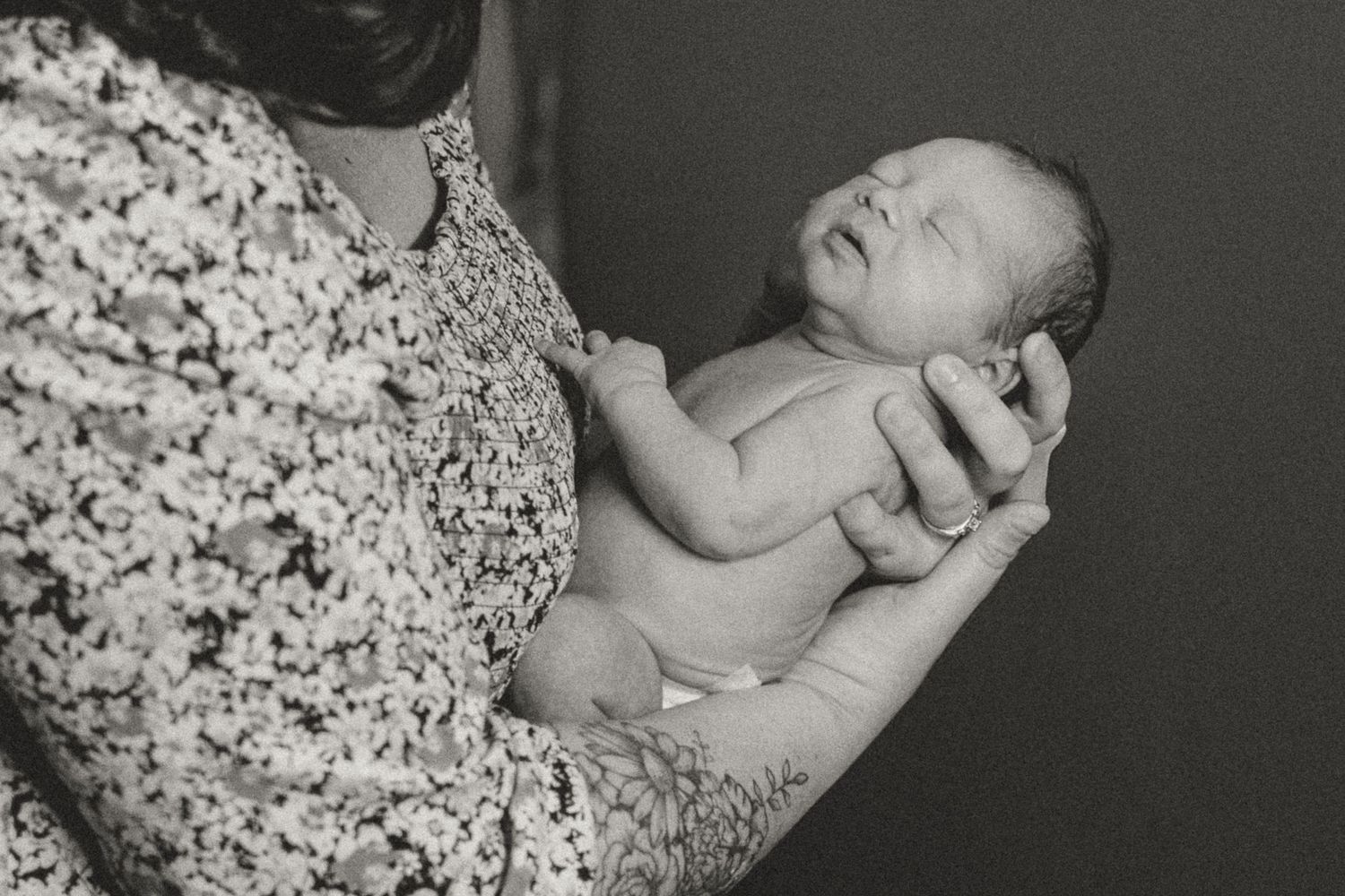 Black and white photo of a newborn baby cradled in adult hands against a floral dress.