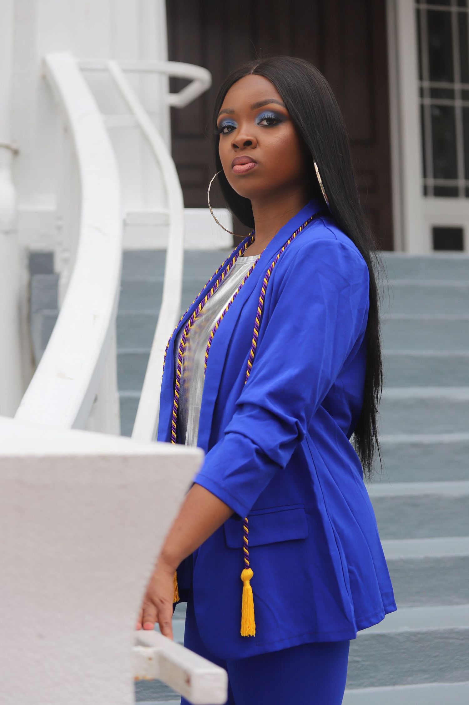 Strong educated woman in blue blazer suit with graduation tassel posing on steps.
