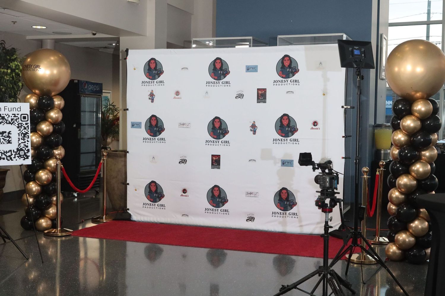 Red carpet photo backdrop with gold balloons and camera setup in event venue.