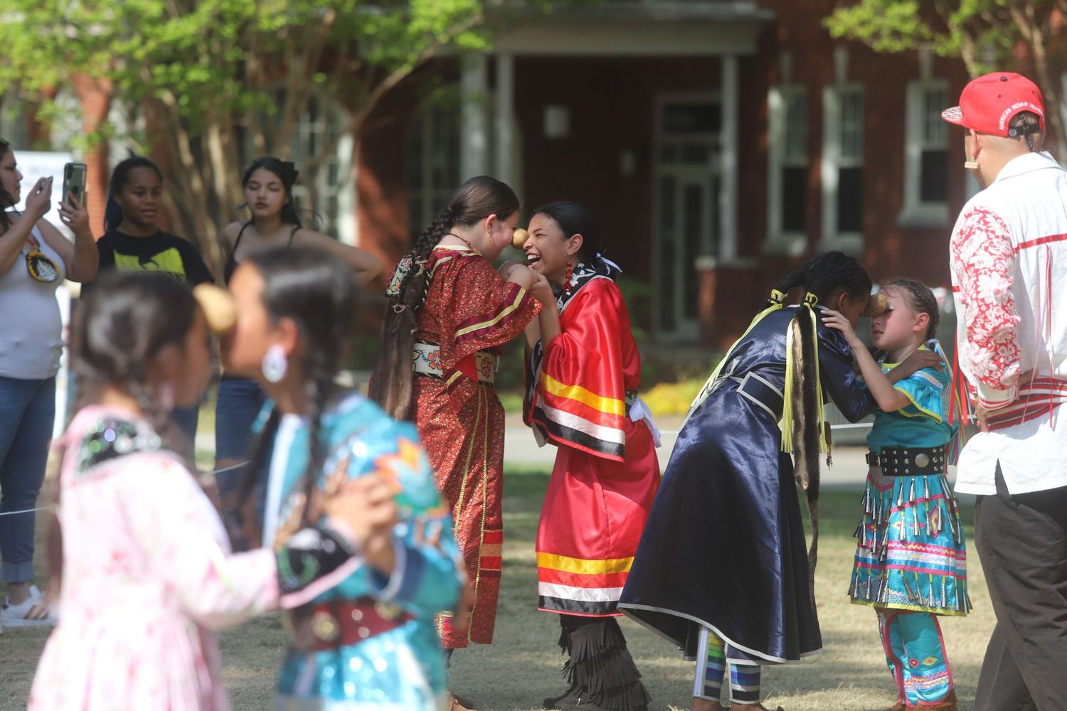 Native American children and adults in traditional regalia at outdoor cultural event.