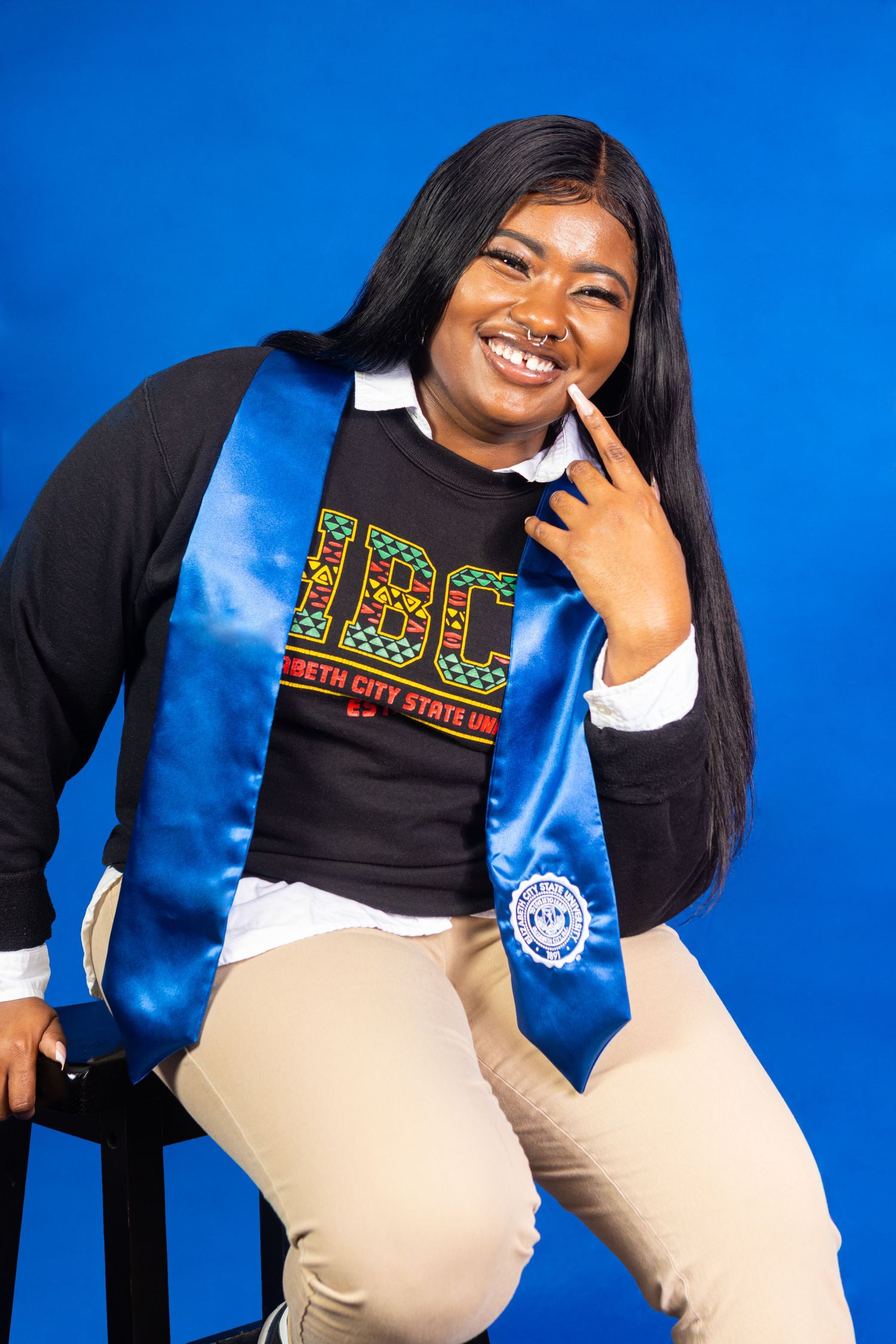 Young College graduated posing leaned on a stool during a portrait session.