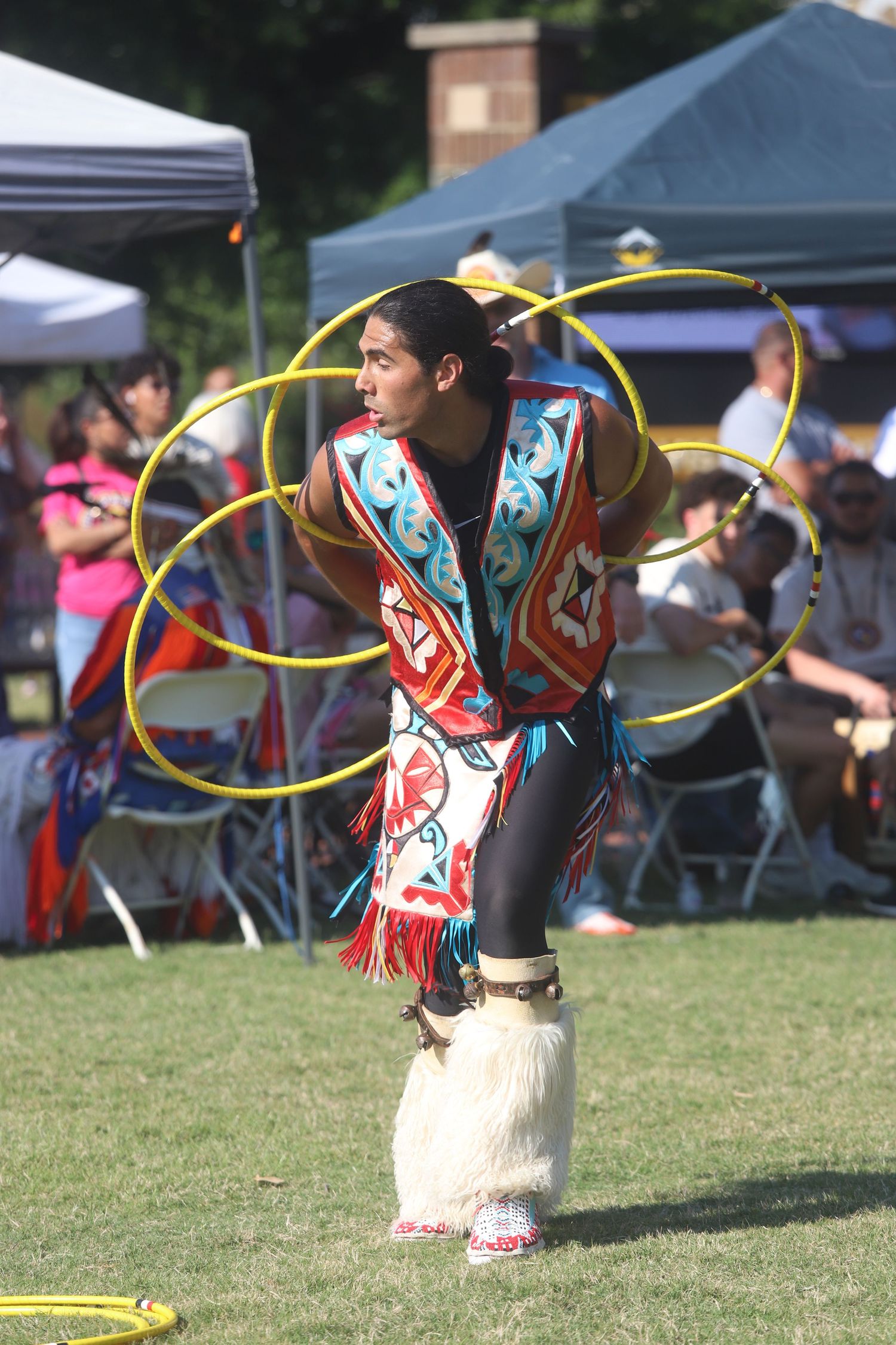 Native American hoop dancer performing with yellow hoops in traditional regalia outdoors.