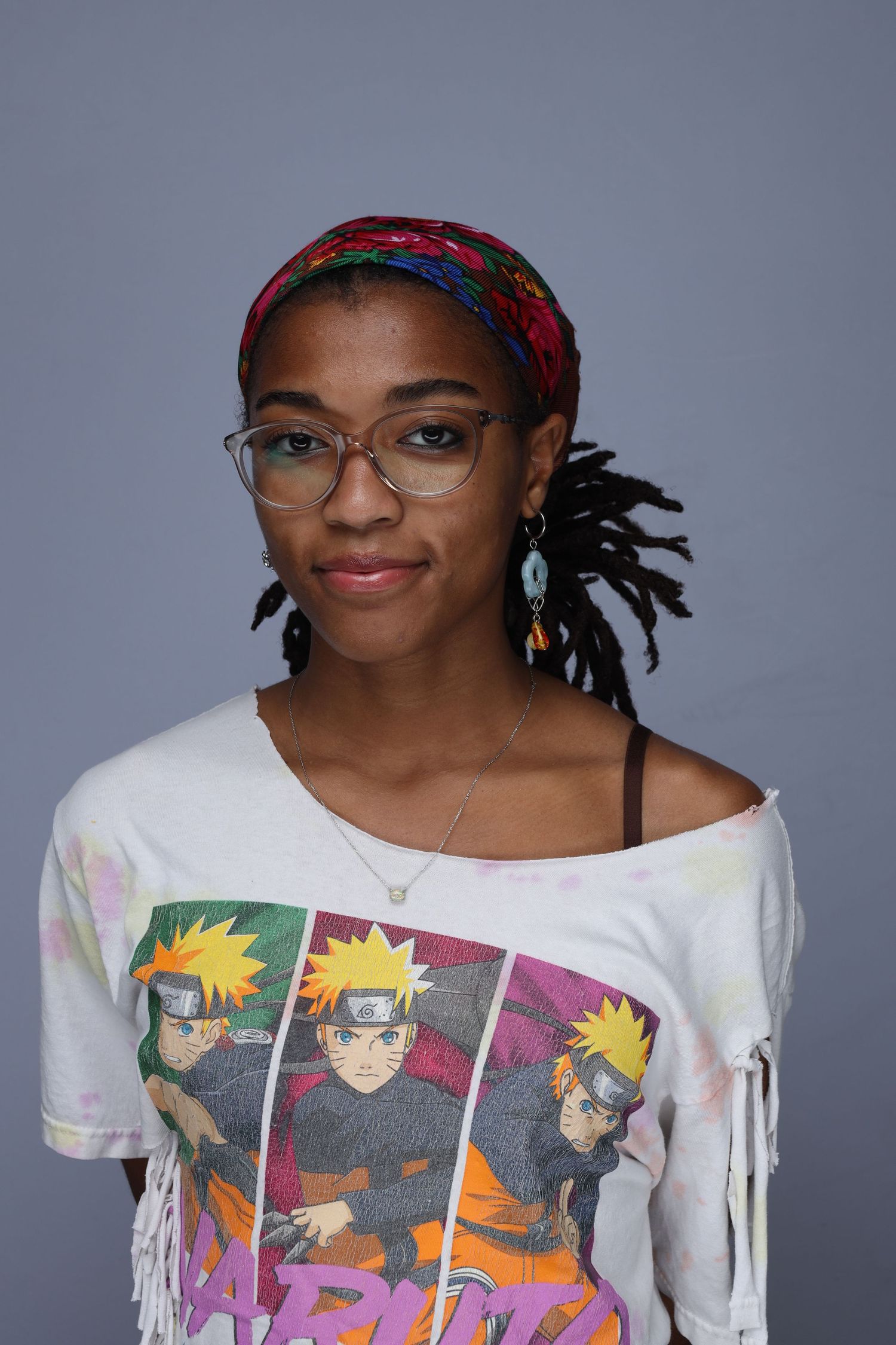 Young woman and in a headband wearing a Naruto graphic tee and glasses poses for portrait.
