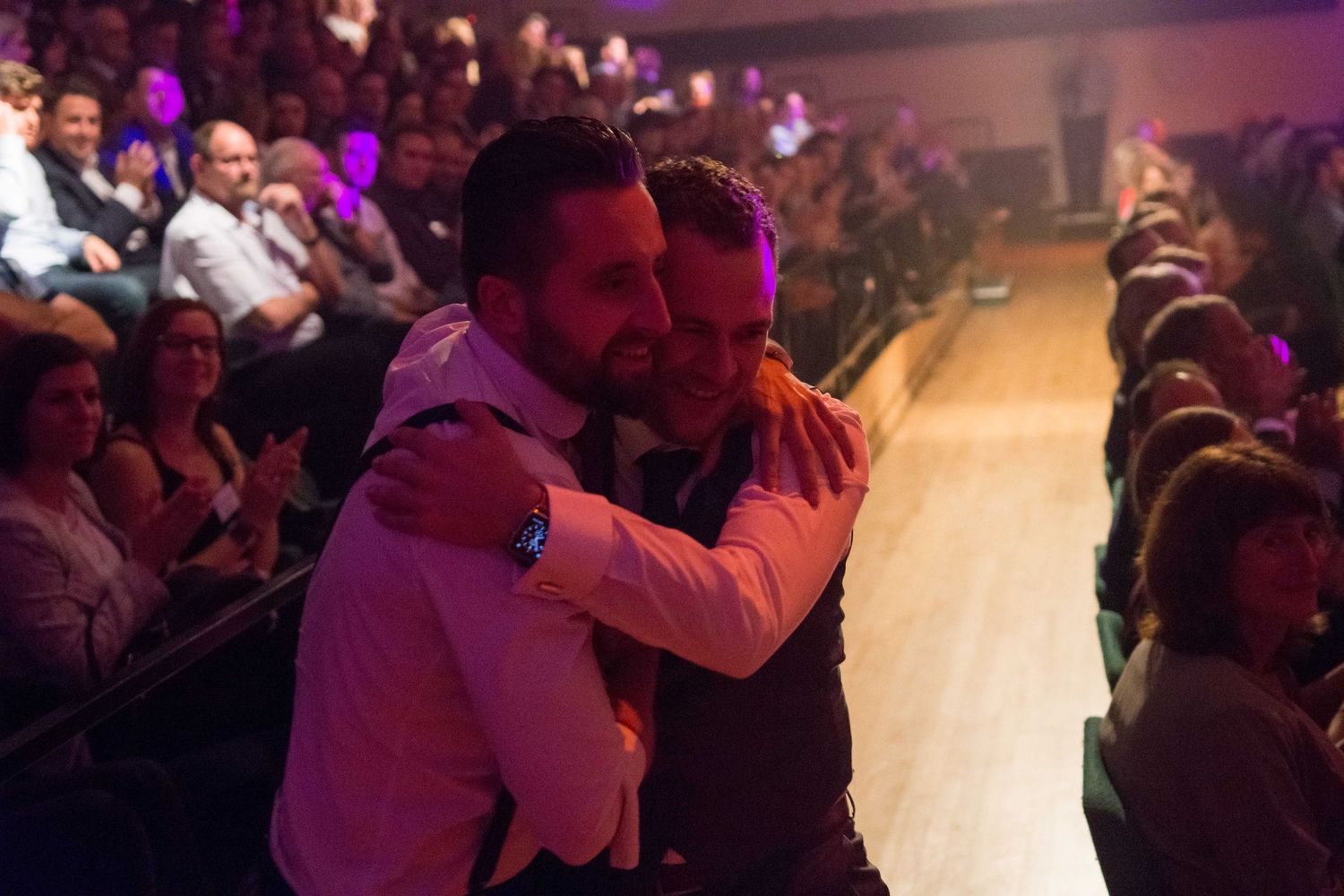 Two men sharing a warm embrace heading to the stage in front of a seated audience at an the south wiltshire business of the year awards