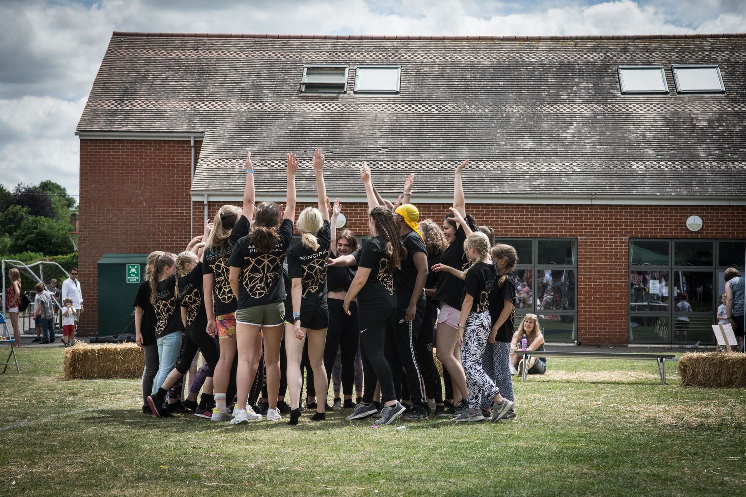 Group of young people from Panthera dance school dressed in black shirts huddling together on a grass field outdoors.