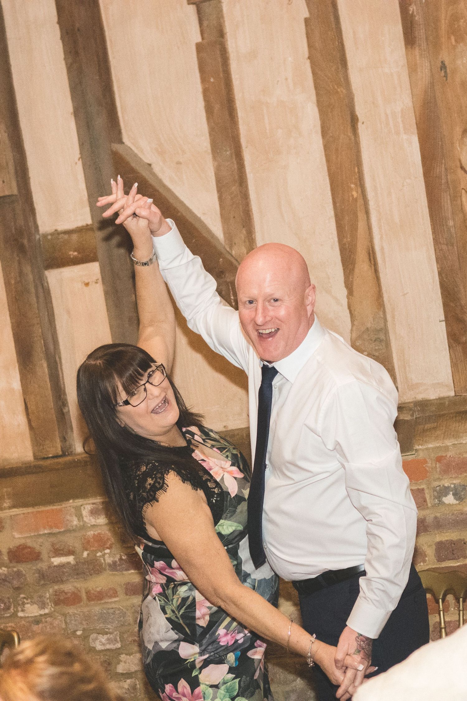 Couple dancing energetically in rustic barn venue with exposed timber beams at wedding reception.