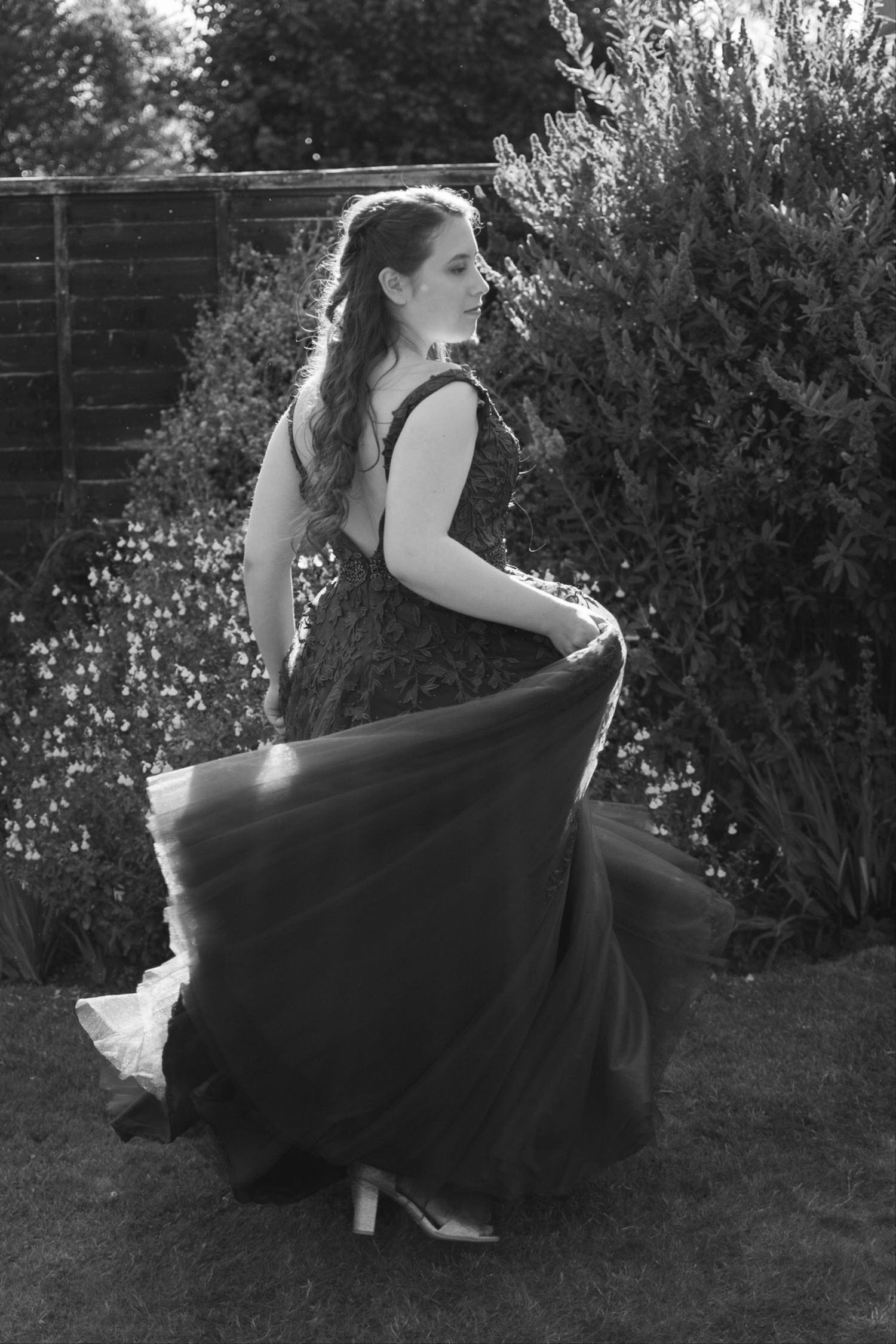 Black and white photo of a woman in an elegant ball gown twirling in a garden setting.