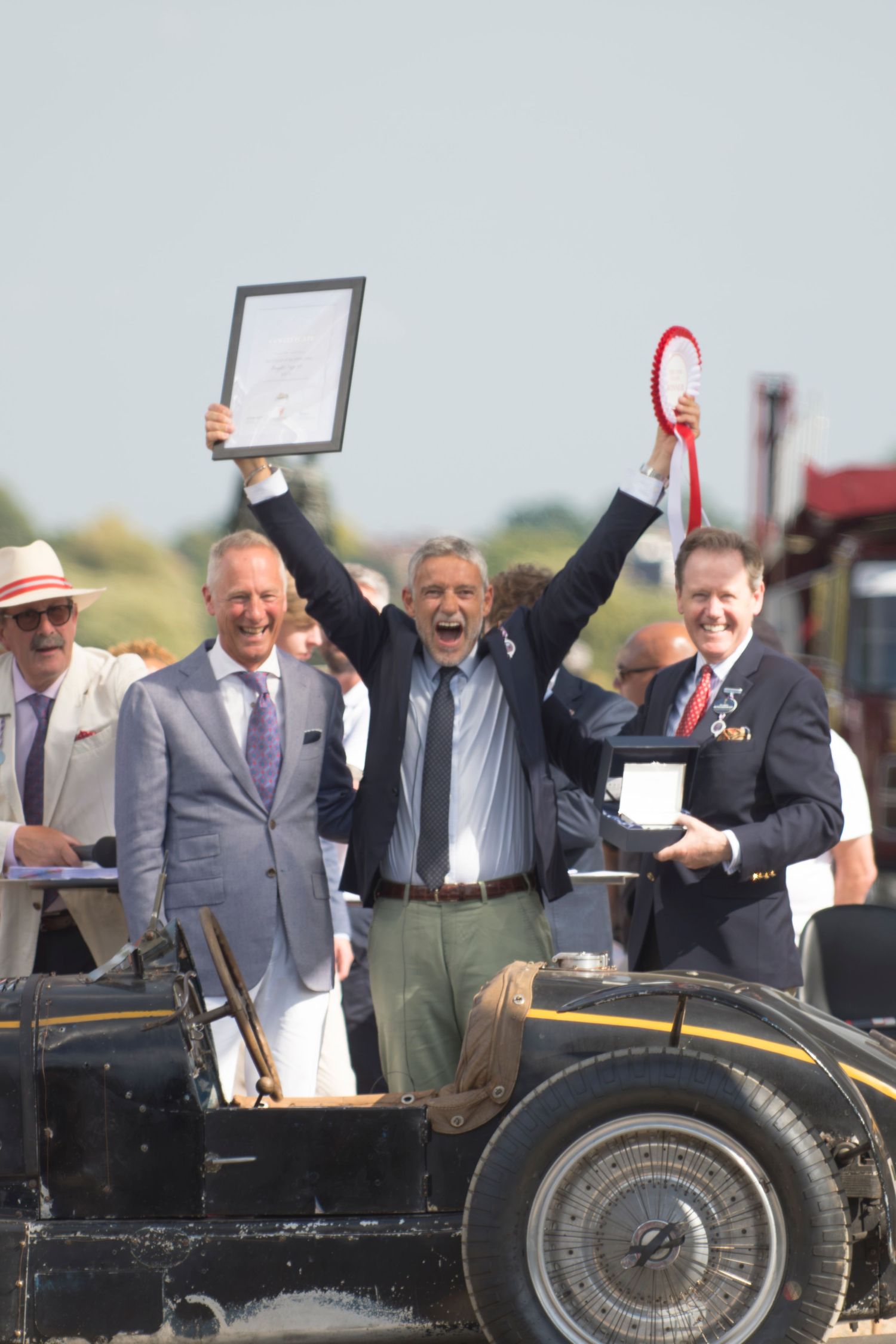 A jubilant Fritz Burkard raises a trophy and ribbon in celebration at Concours of elegance.