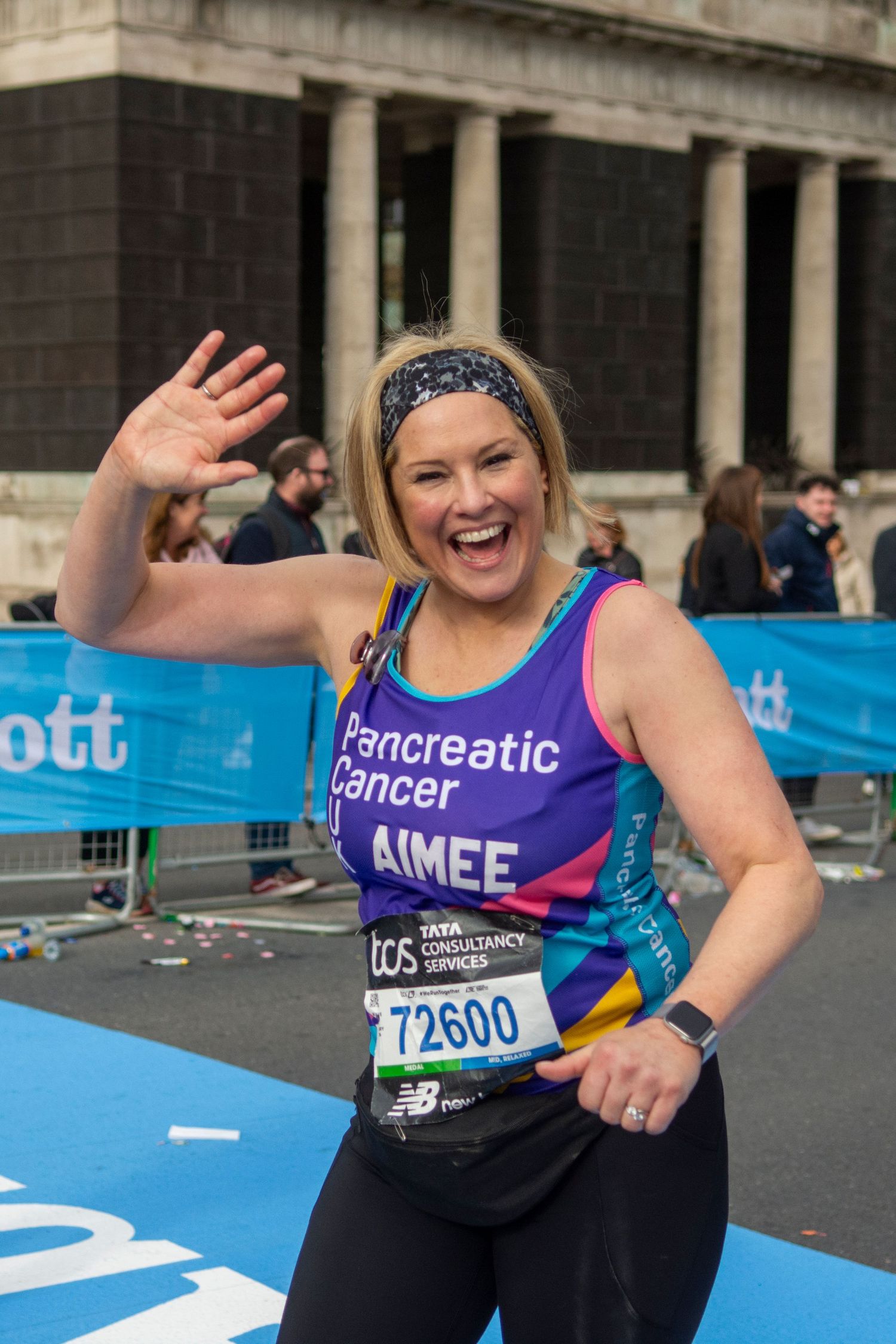 Smiling woman in Pancreatic Cancer charity vest waves at London Marathon finish line.