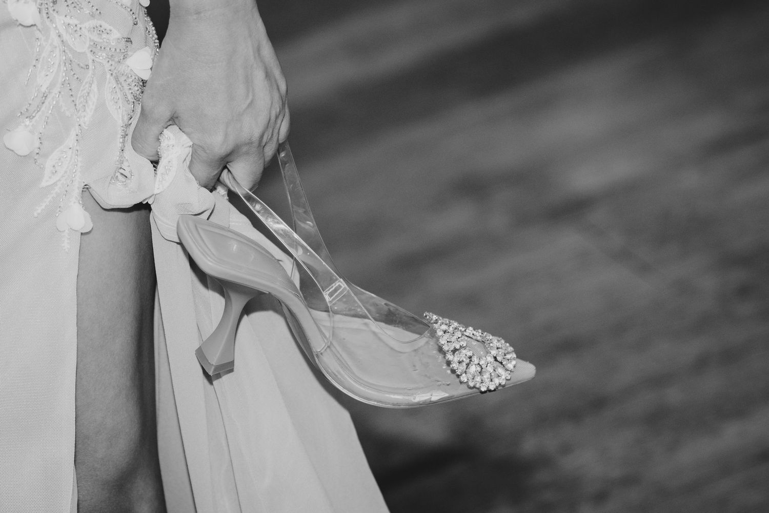 Black and white photo of a bride holding pearl-embellished heels in her wedding dress.