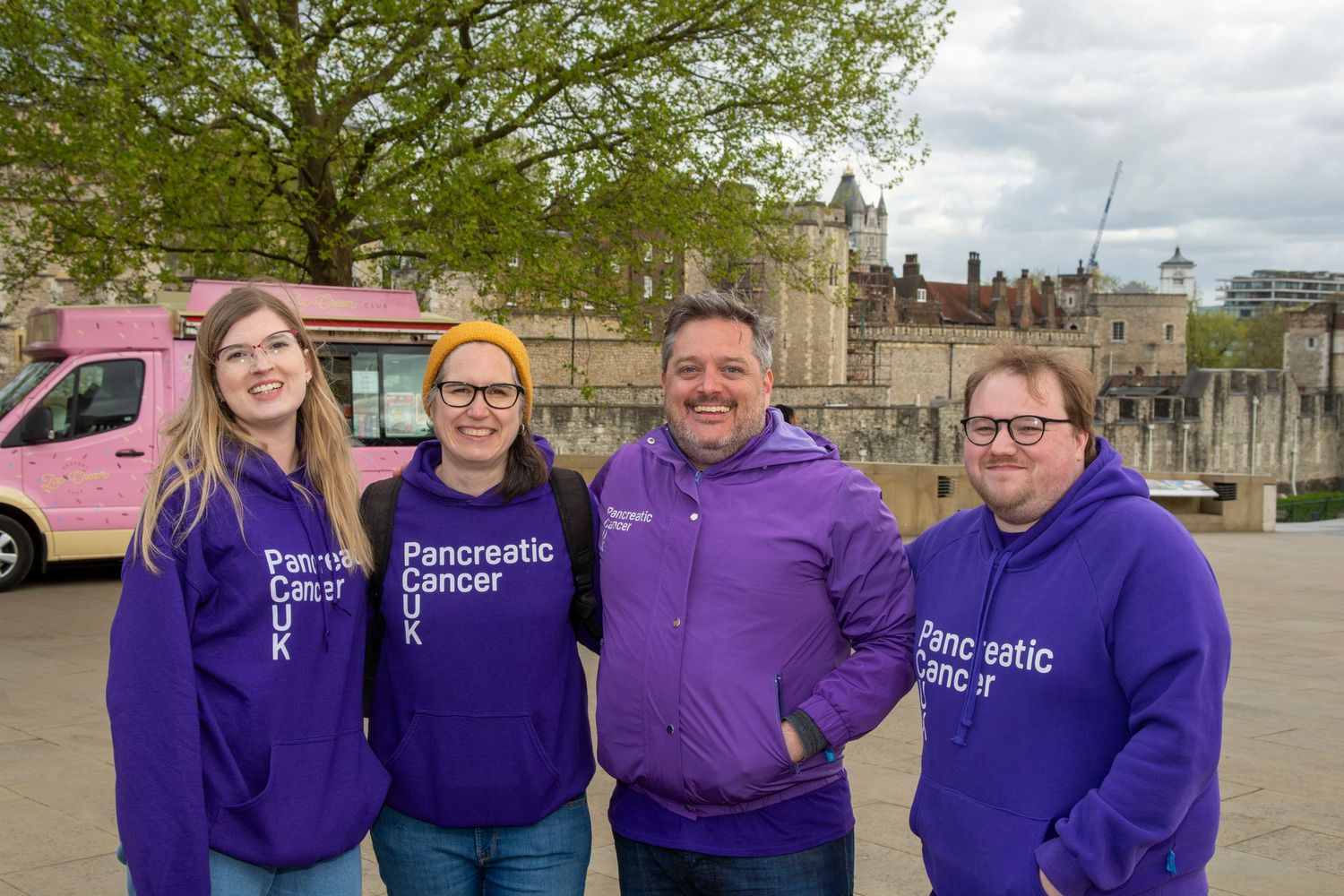 Four people in purple Pancreatic Cancer UK hoodies pose near Tower of London.