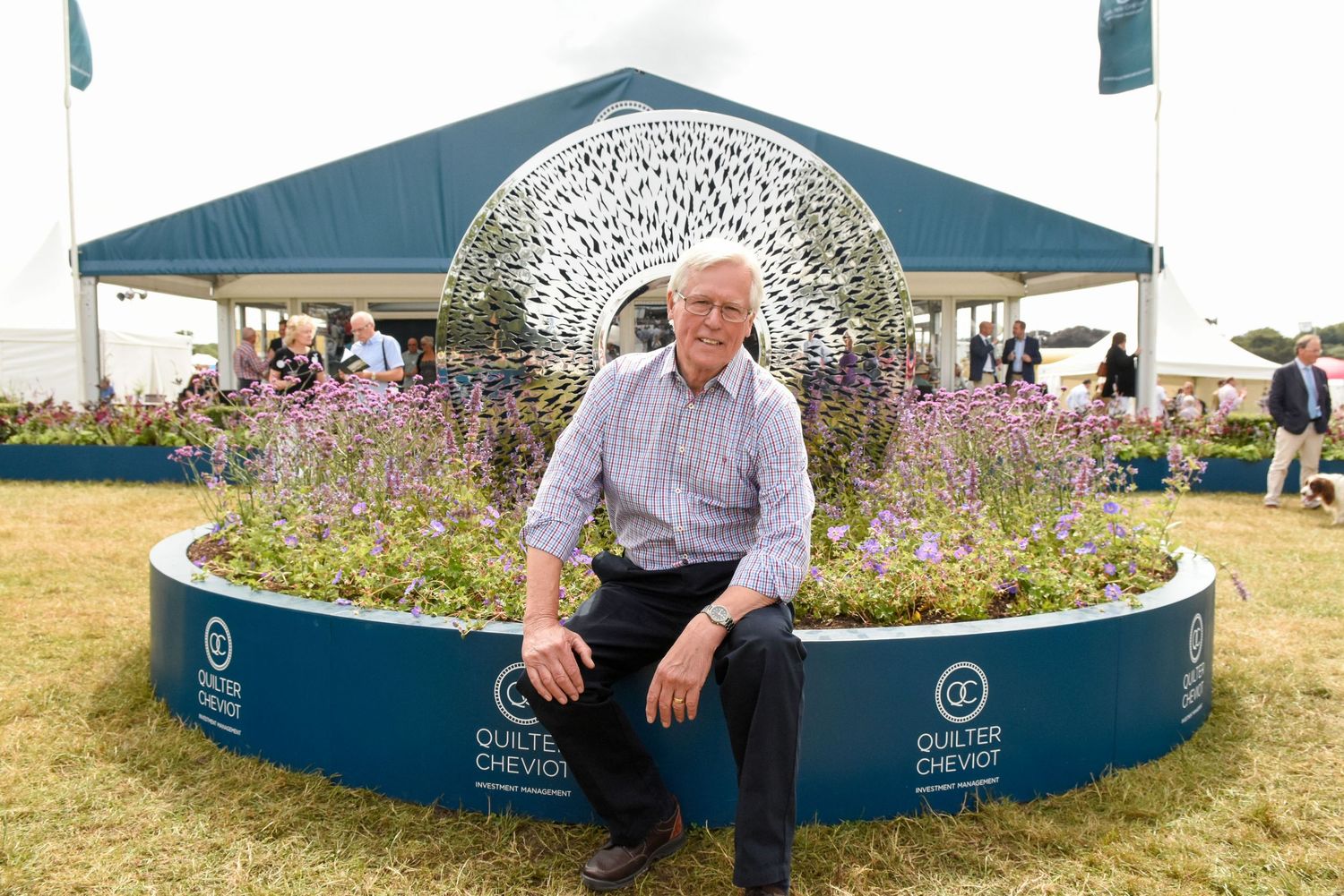 BBC's Jihn Craven sitting beside a decorative metal dome sculpture at a Quilter Cheviot outdoor garden event.