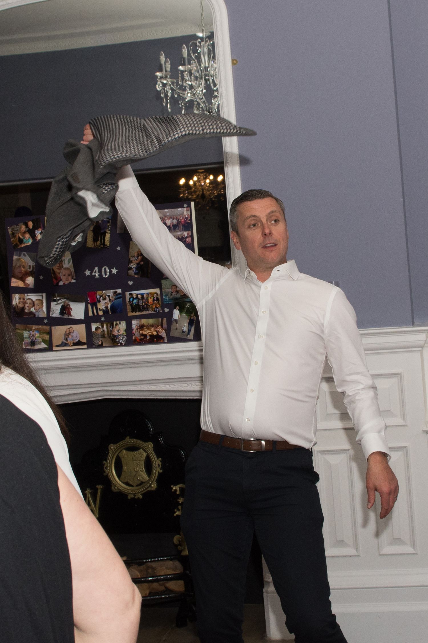 Man in white shirt raises striped hat at indoor birthday party celebration.