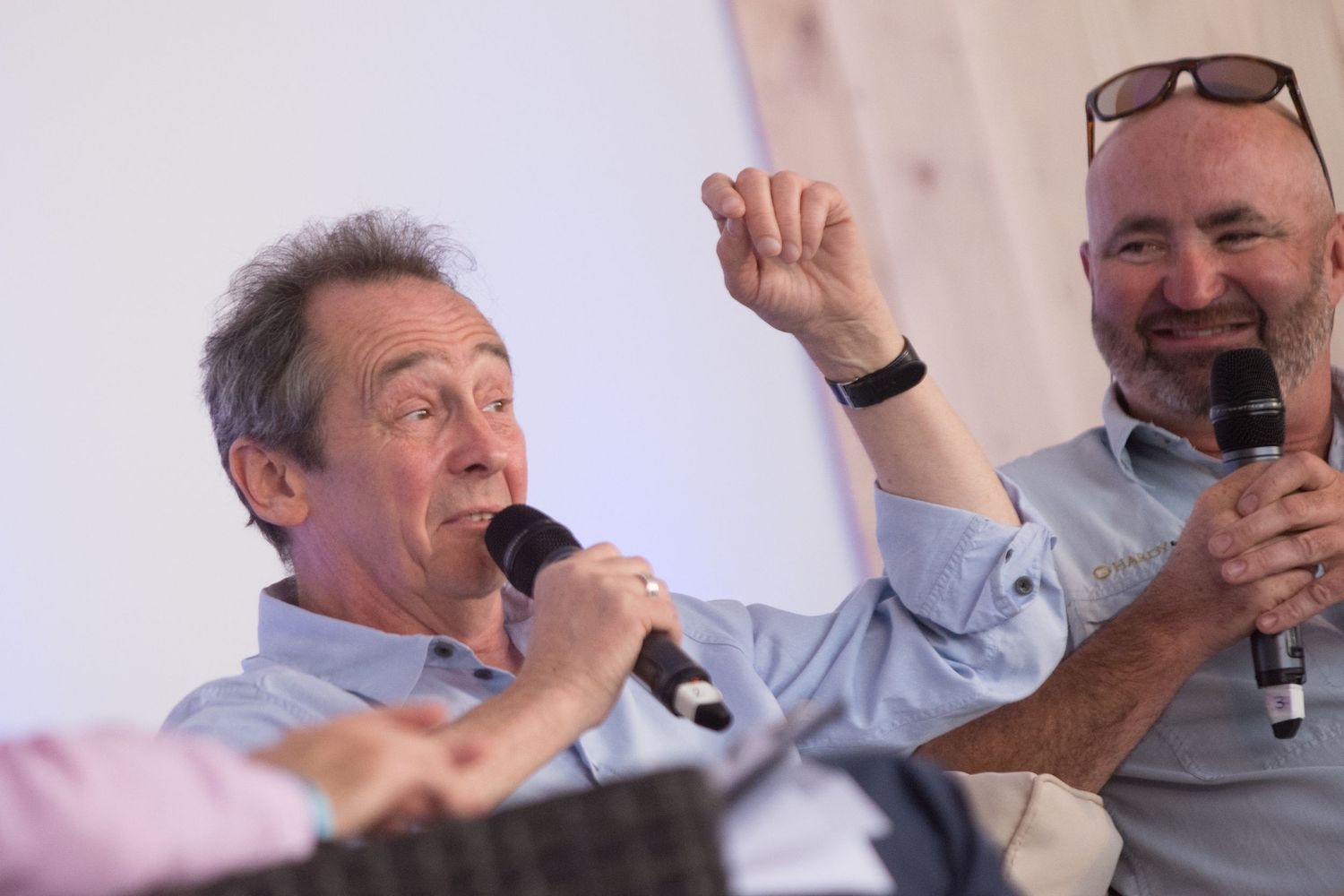Paul Whitehouse speaking animatedly into microphones during a lively panel discussion at an outdoor event.