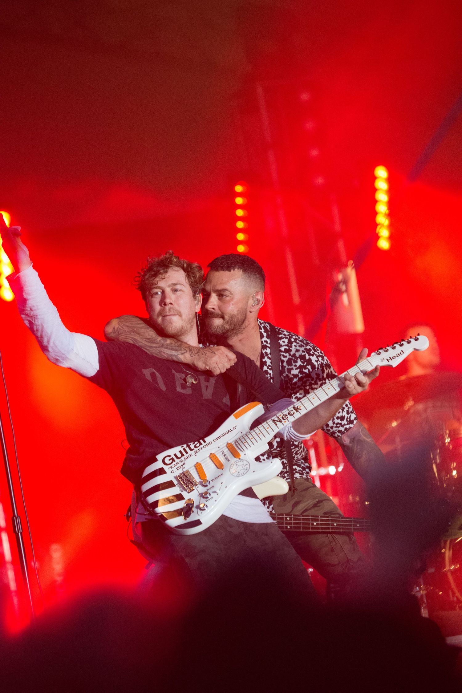Busted's James Bourne & Matt Willis embracing on stage under dramatic red lights during a live concert performance.