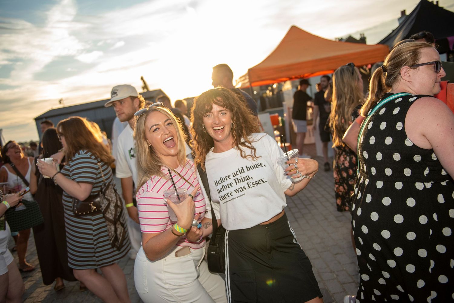 Two women laugh and pose together at Essex Pizza festival, one wearing a printed white t-shirt.