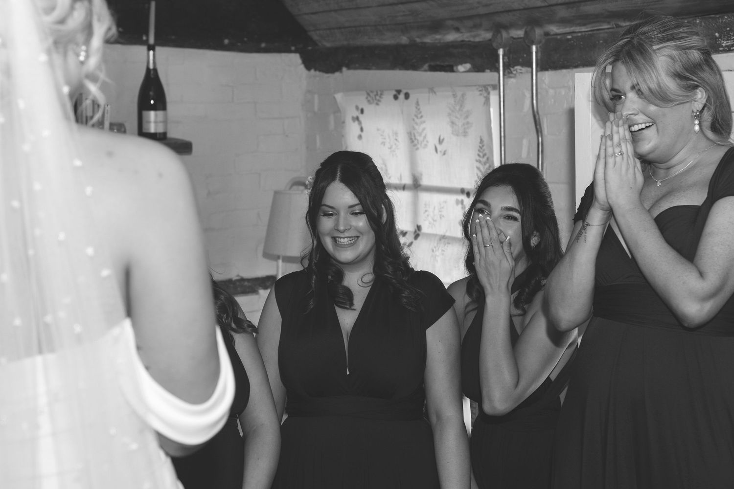 Black and white photo of emotional bridesmaids reacting with joy and tears seeing bride in wedding dress for first time.