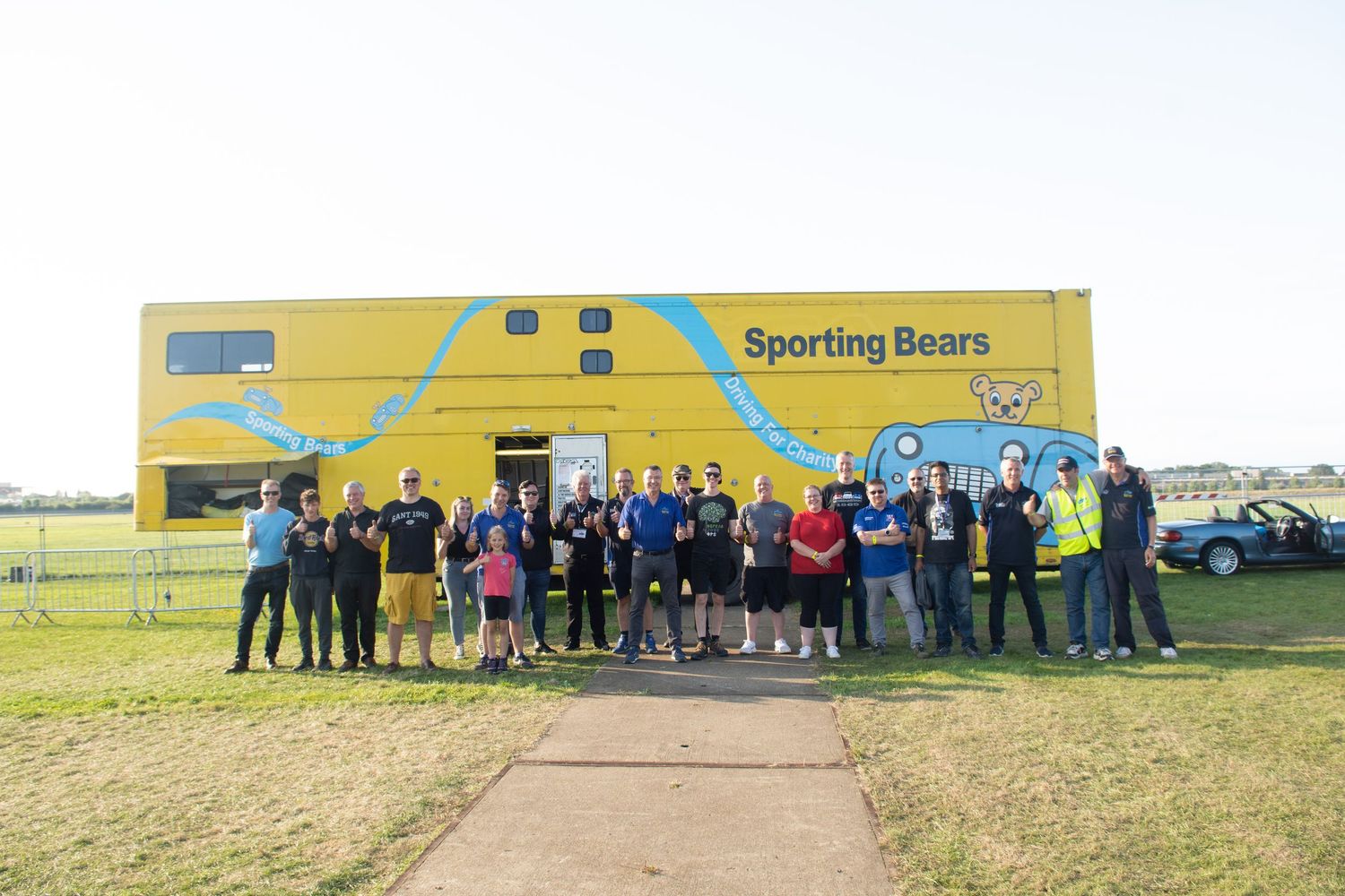 Group of people posing outside the bright yellow Sporting Bears Truck at the British Motor show