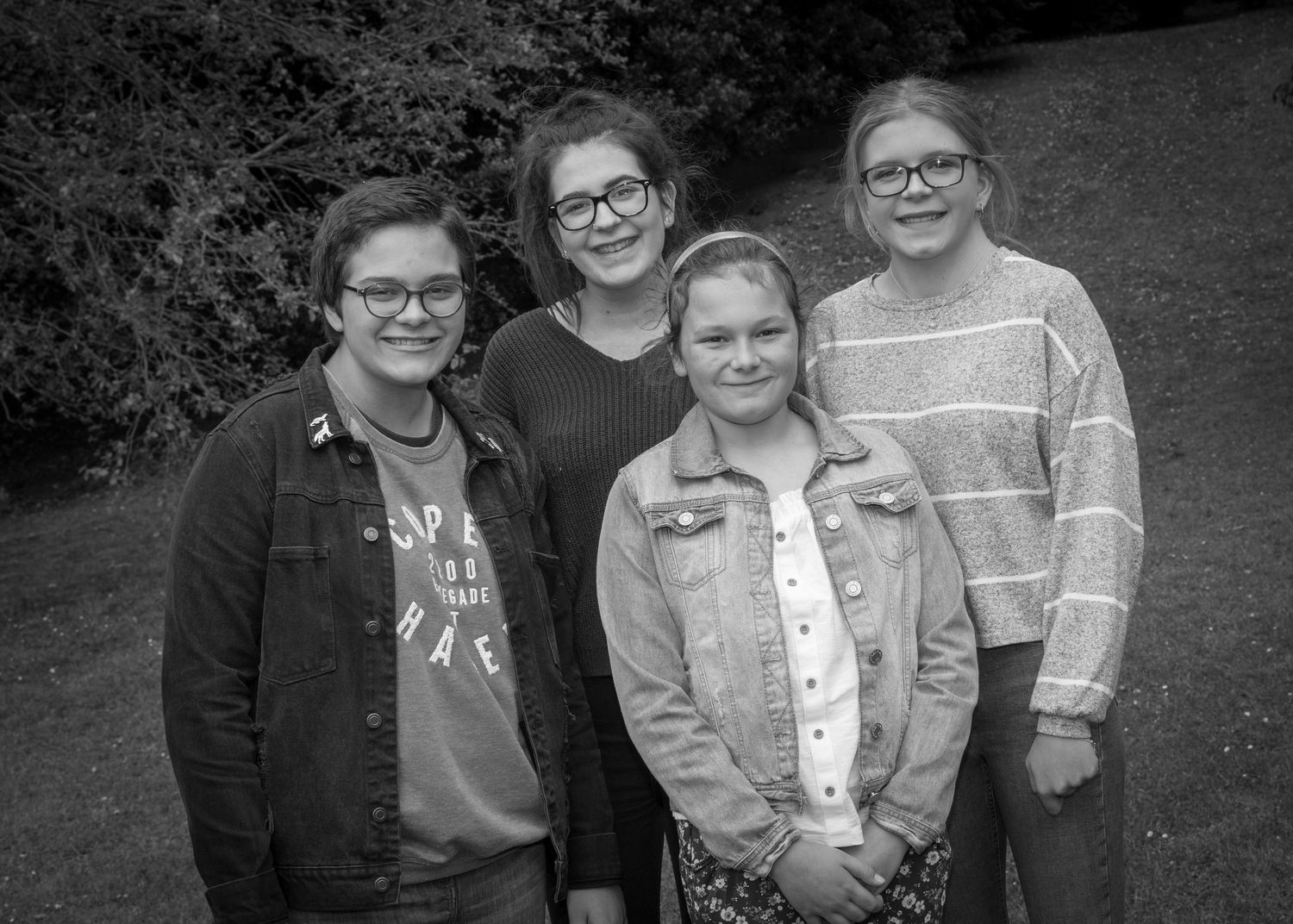 Four girls posing together outdoors in a black and white photo, smiling at the camera.