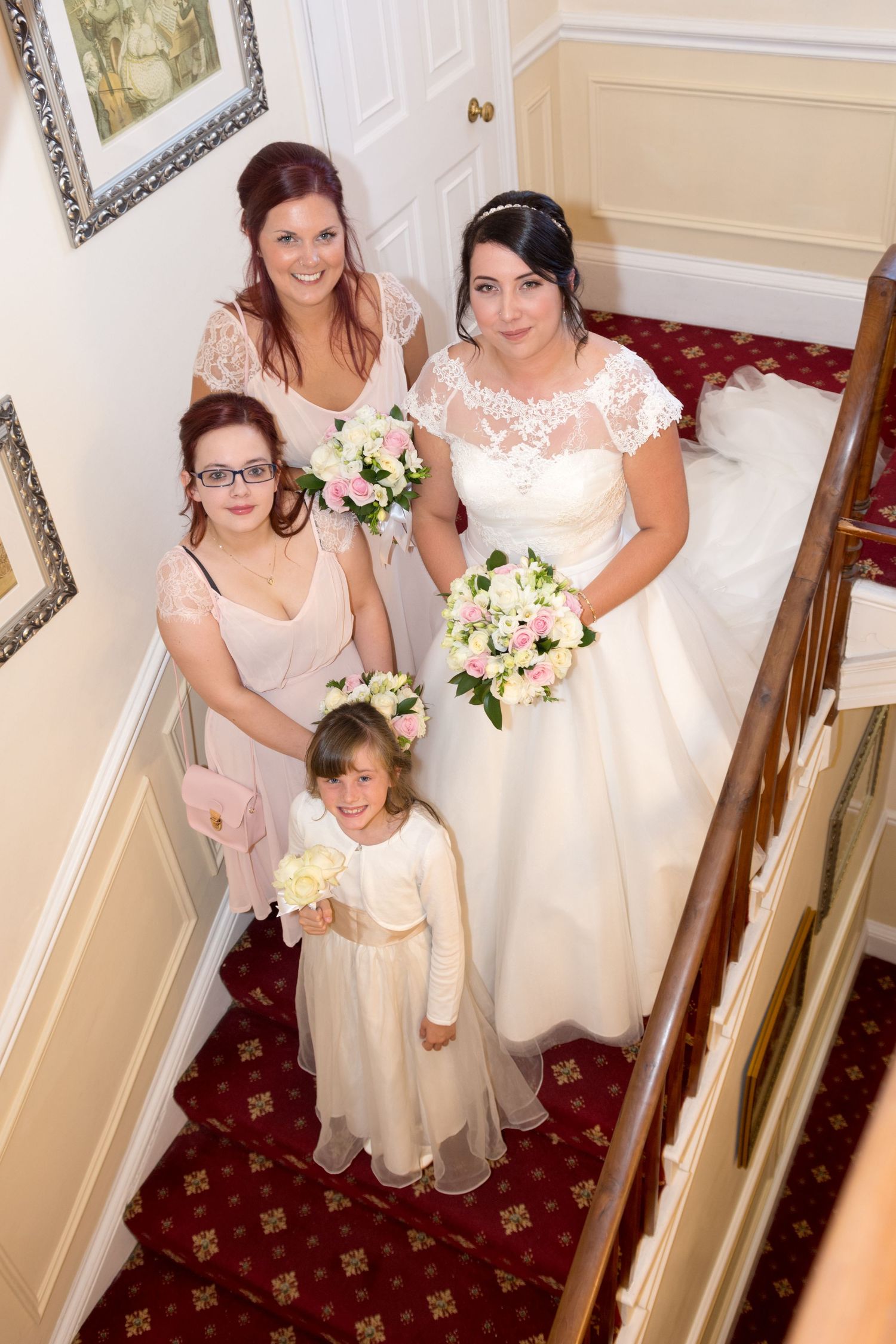 Bride with bridesmaids and flower girl posing on a grand staircase holding pink and white bouquets.