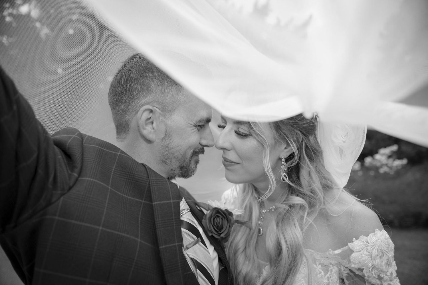 Black and white photo of bride and groom sharing an intimate moment under a flowing wedding veil.