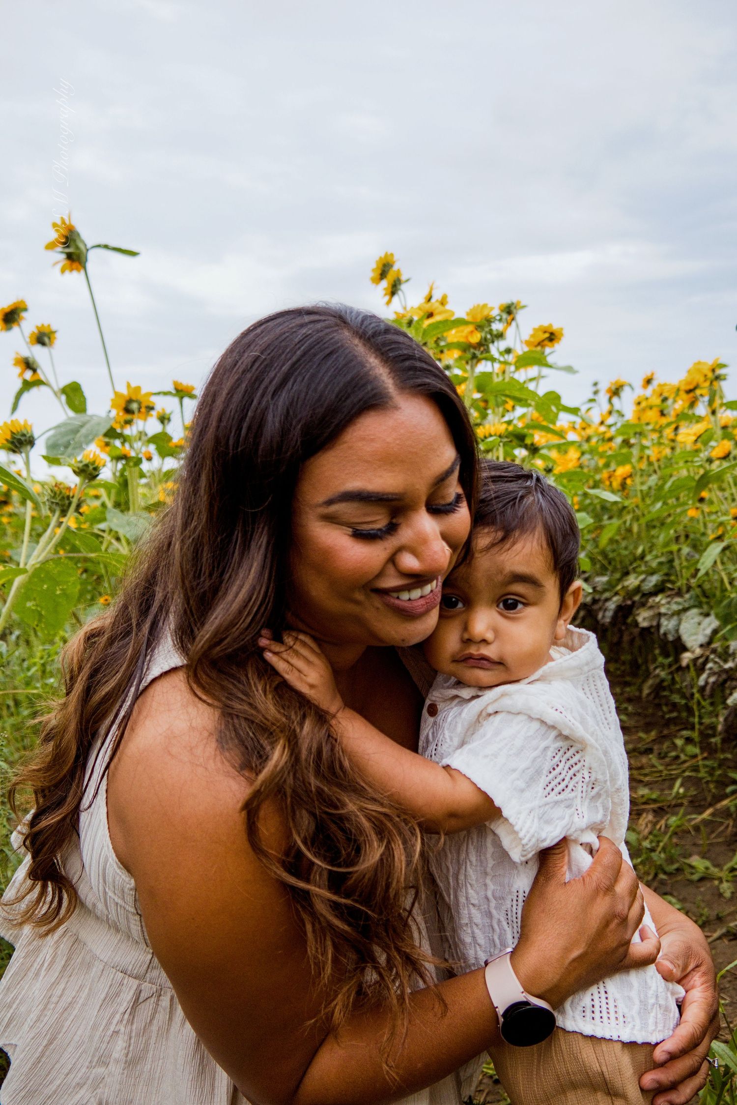 Family hugging in front of bright yellow sunflowers at Pingle's Farm Market