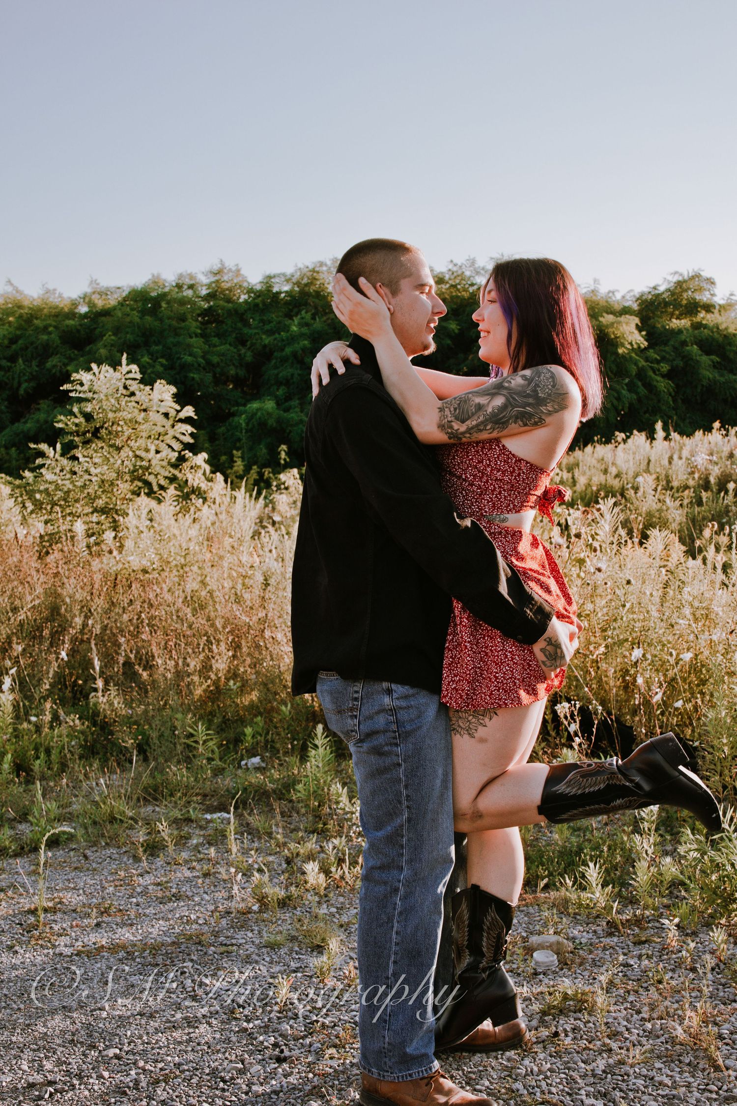 A couple embraces and gazes at each other lovingly in a golden field at sunset.