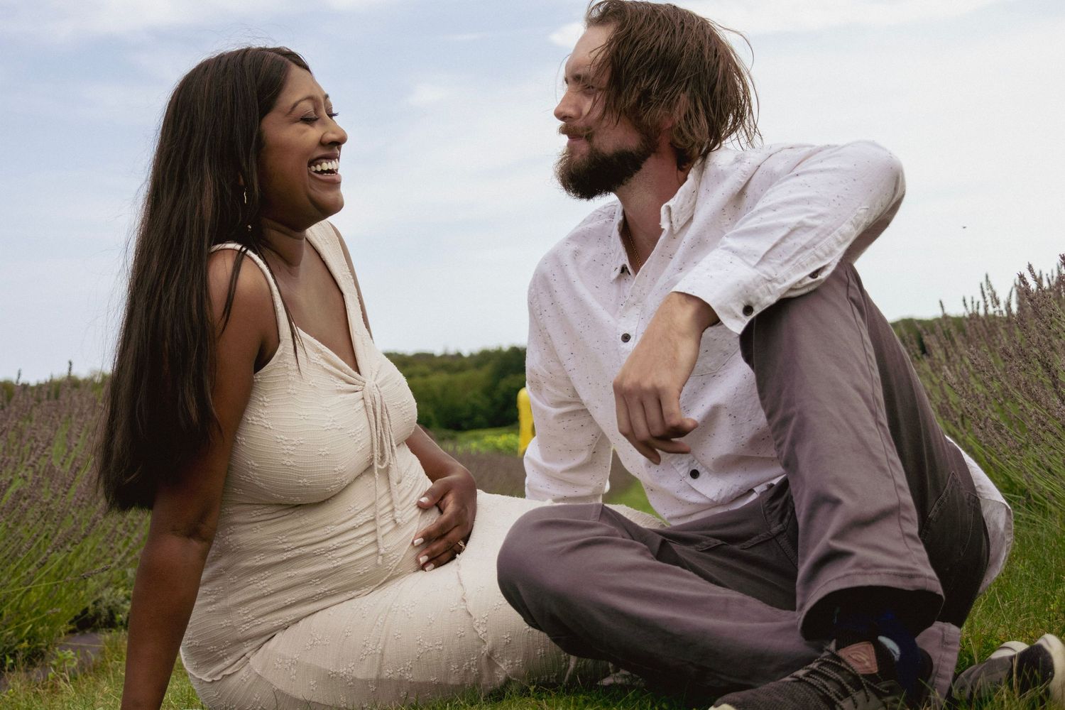 A couple sharing a joyful moment in a lavender field, woman in cream dress and bearded man in white shirt.
