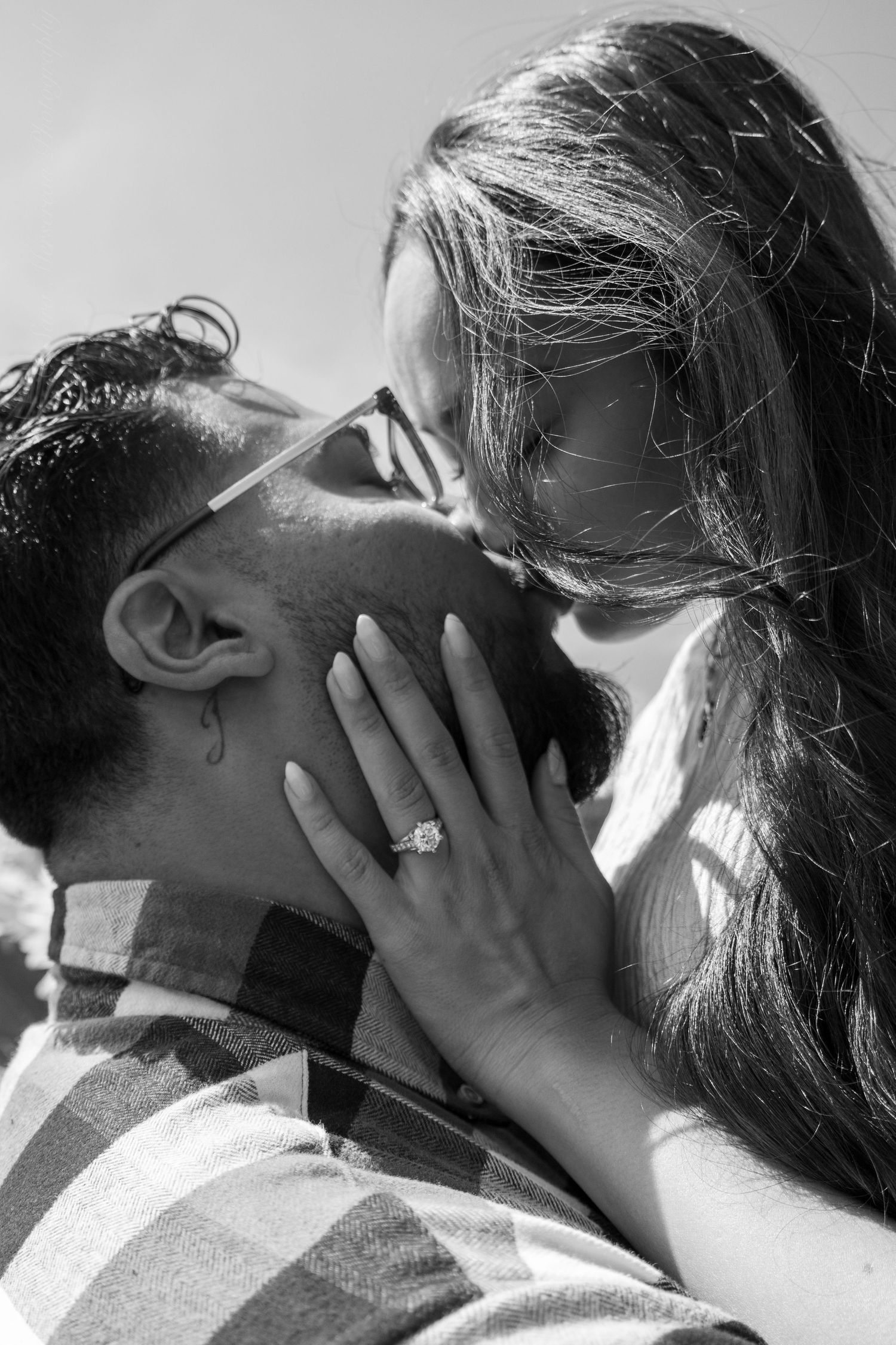 Black and white close-up of a couple kissing, woman displaying a diamond engagement ring.