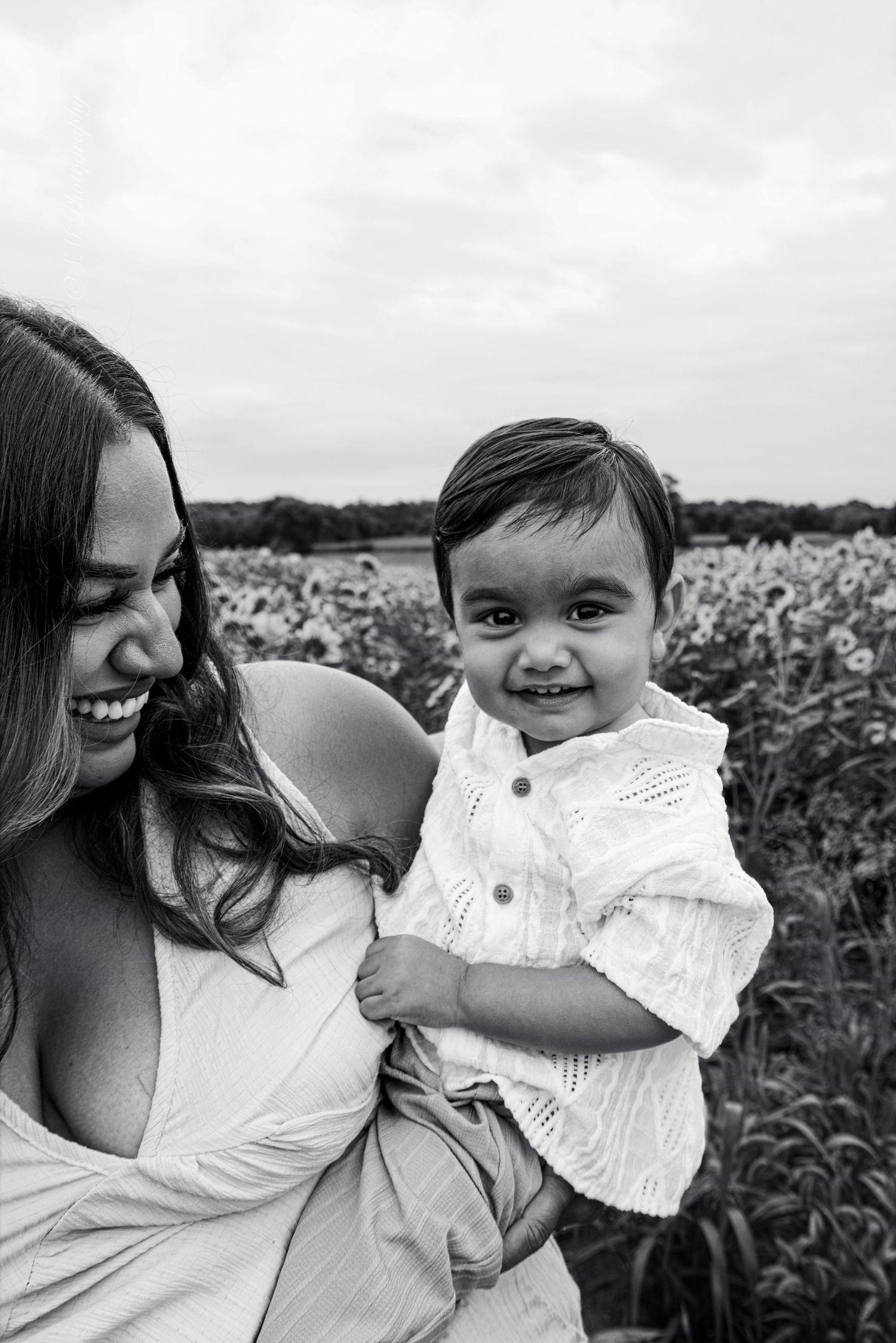Black and white portrait of a smiling mother holding her cheerful baby in a sunflower field.
