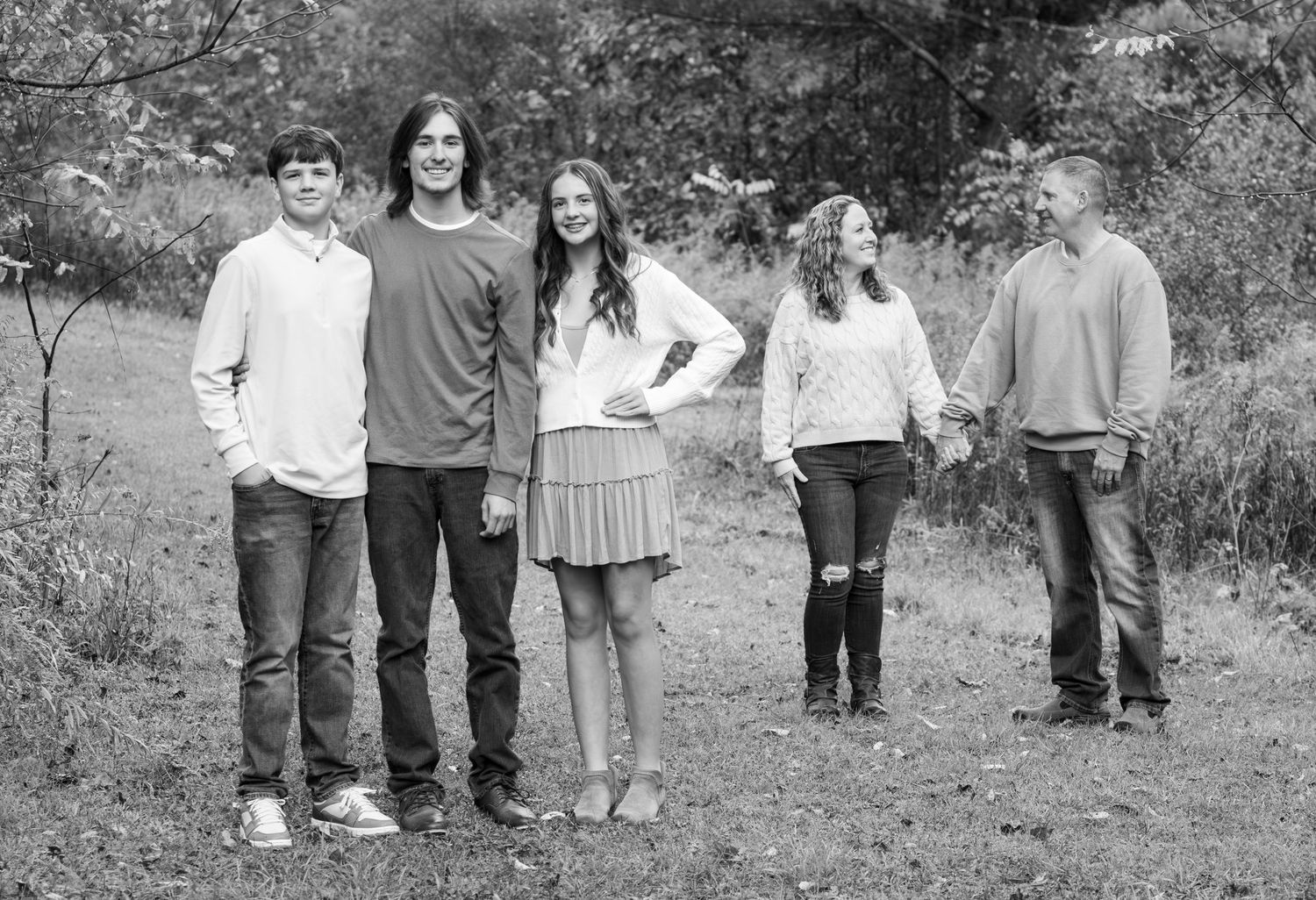 Black and white family portrait of five people standing in an autumn outdoor setting.